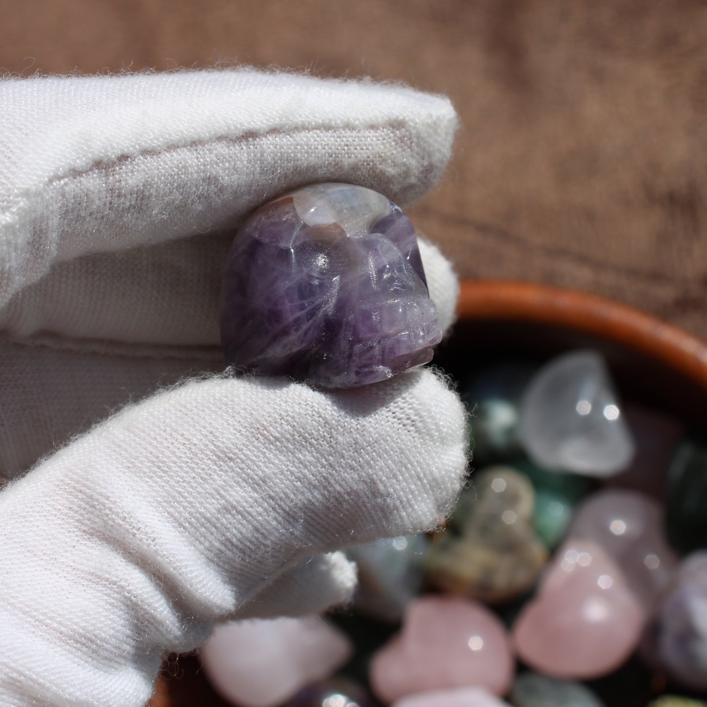 Hand holding a polished amethyst gemstone sugar skull carving with a colorful assortment in the background