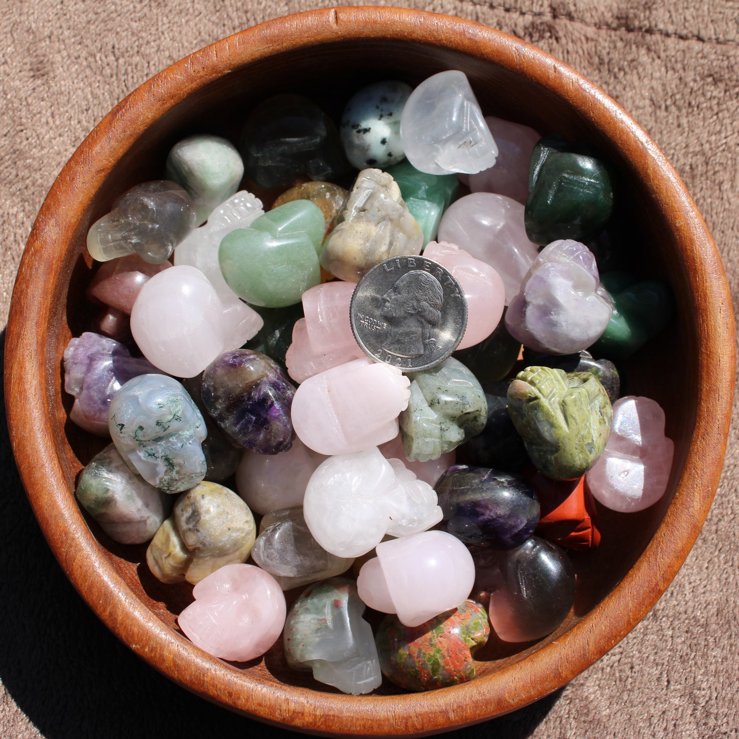 Assorted Gemstone Sugar Skull Carvings in a wooden bowl with a quarter for size reference
