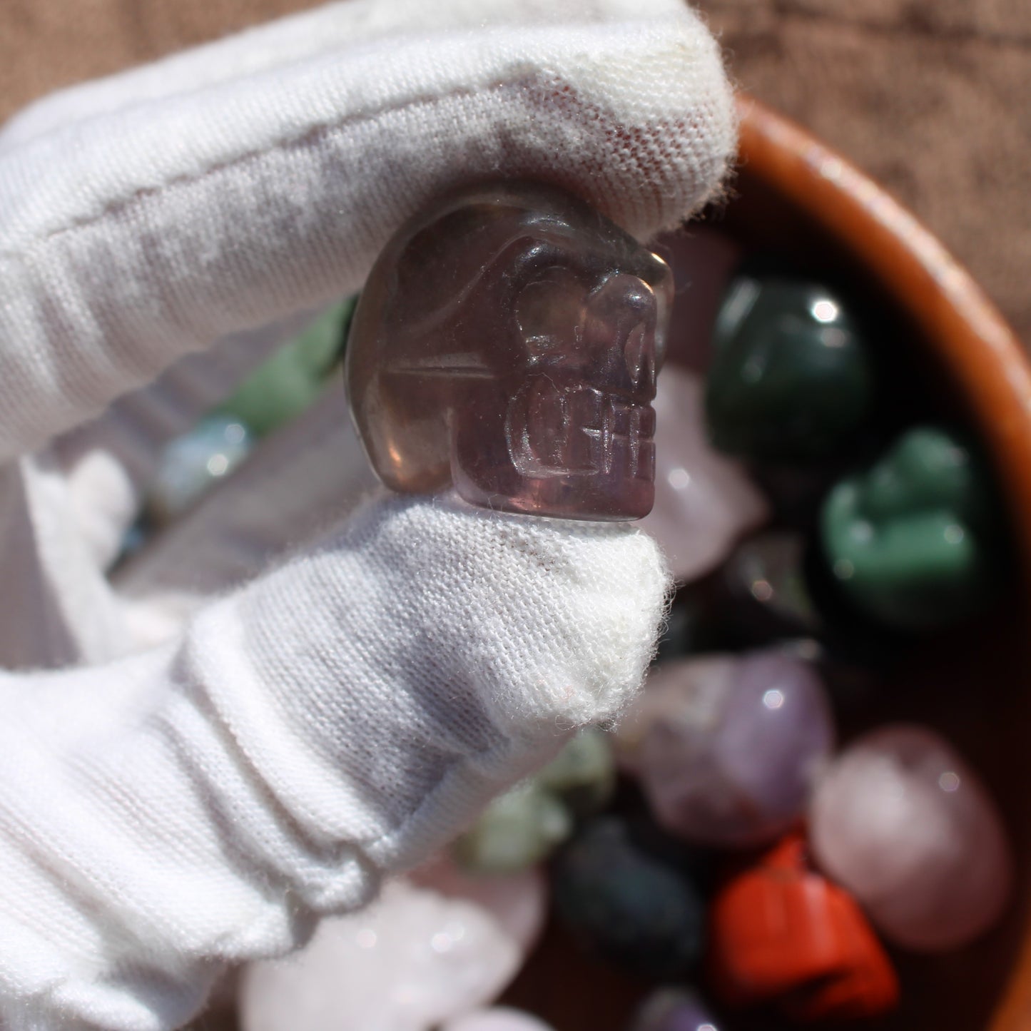 Close-up of a gemstone sugar skull carving held in a gloved hand, showcasing its intricate details and colors