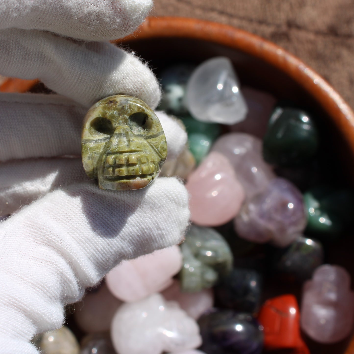 Gemstone Sugar Skull Carvings displayed in a bowl with various colorful crystals