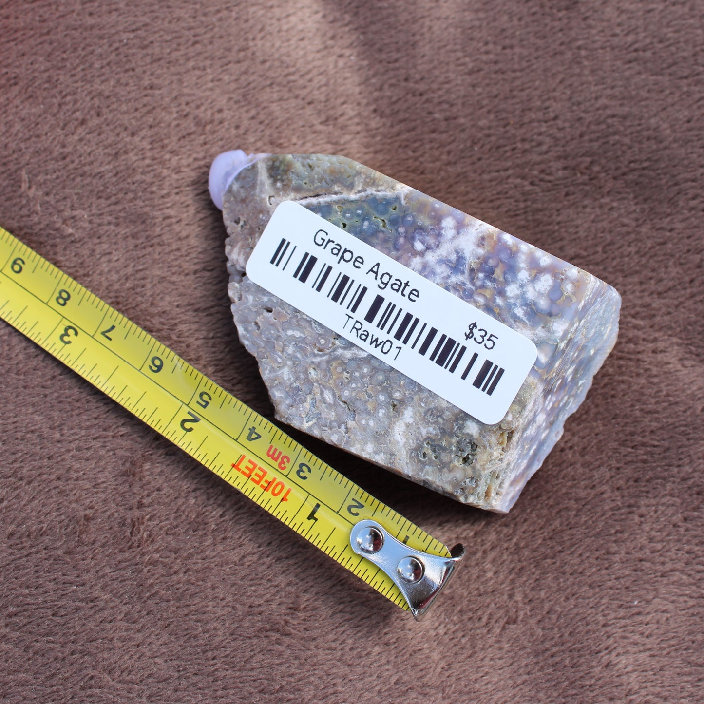 Grape Agate Tower crystal from Different Branches LLC placed next to a yellow measuring tape on a brown surface