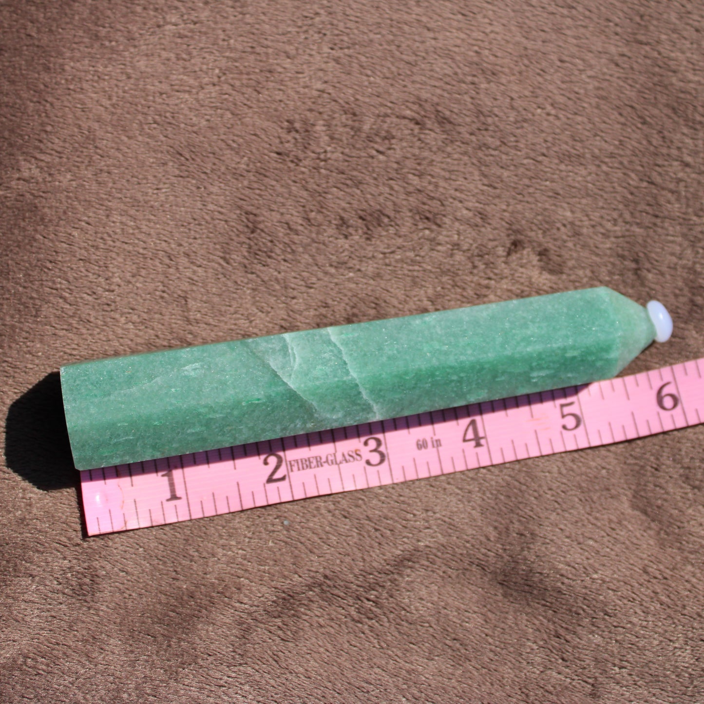 Green Aventurine tower on a beige surface beside a ruler for size reference