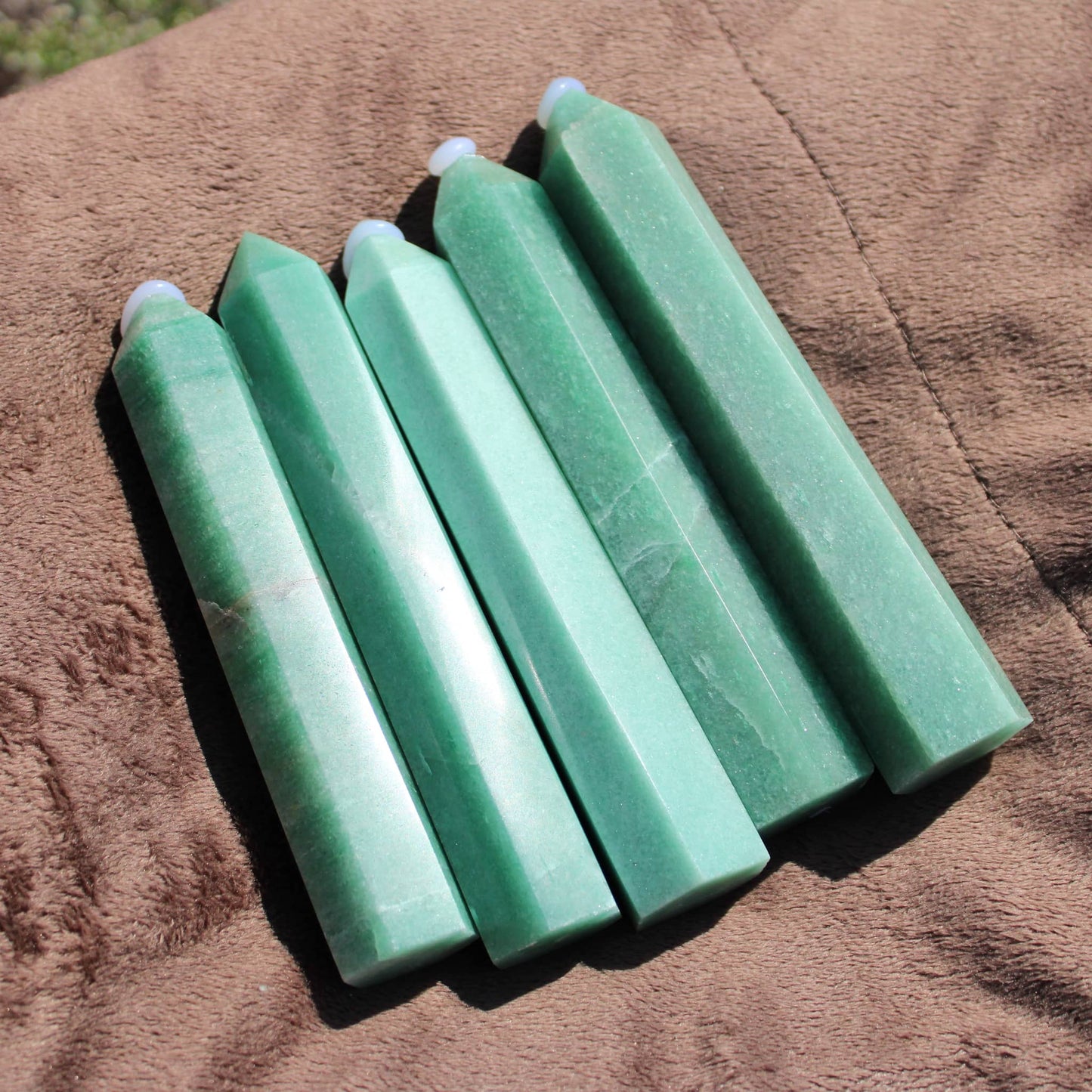 Five Green Aventurine tower crystals arranged on a soft brown surface for healing and decoration