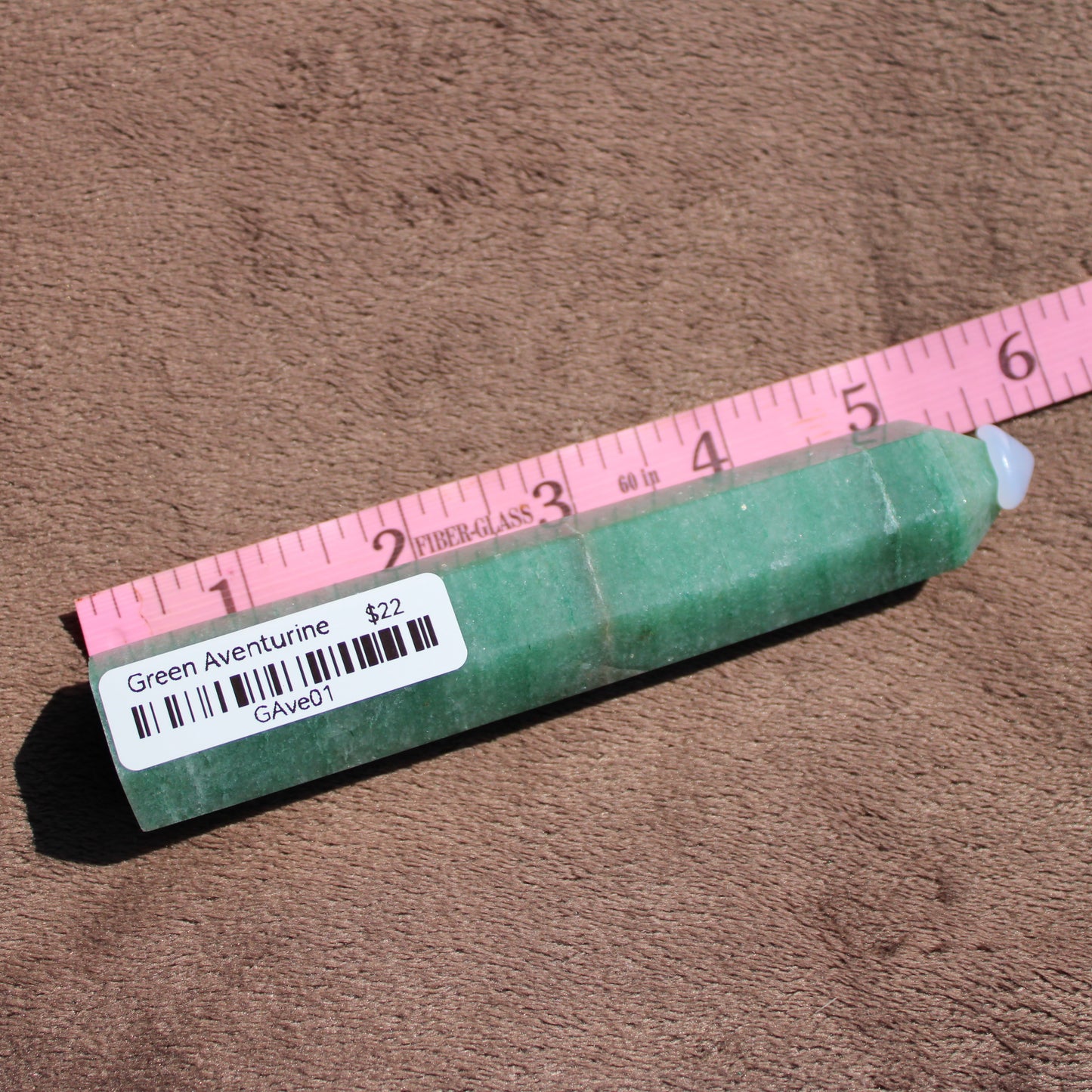 Green Aventurine tower displayed on a brown surface with a ruler for size reference