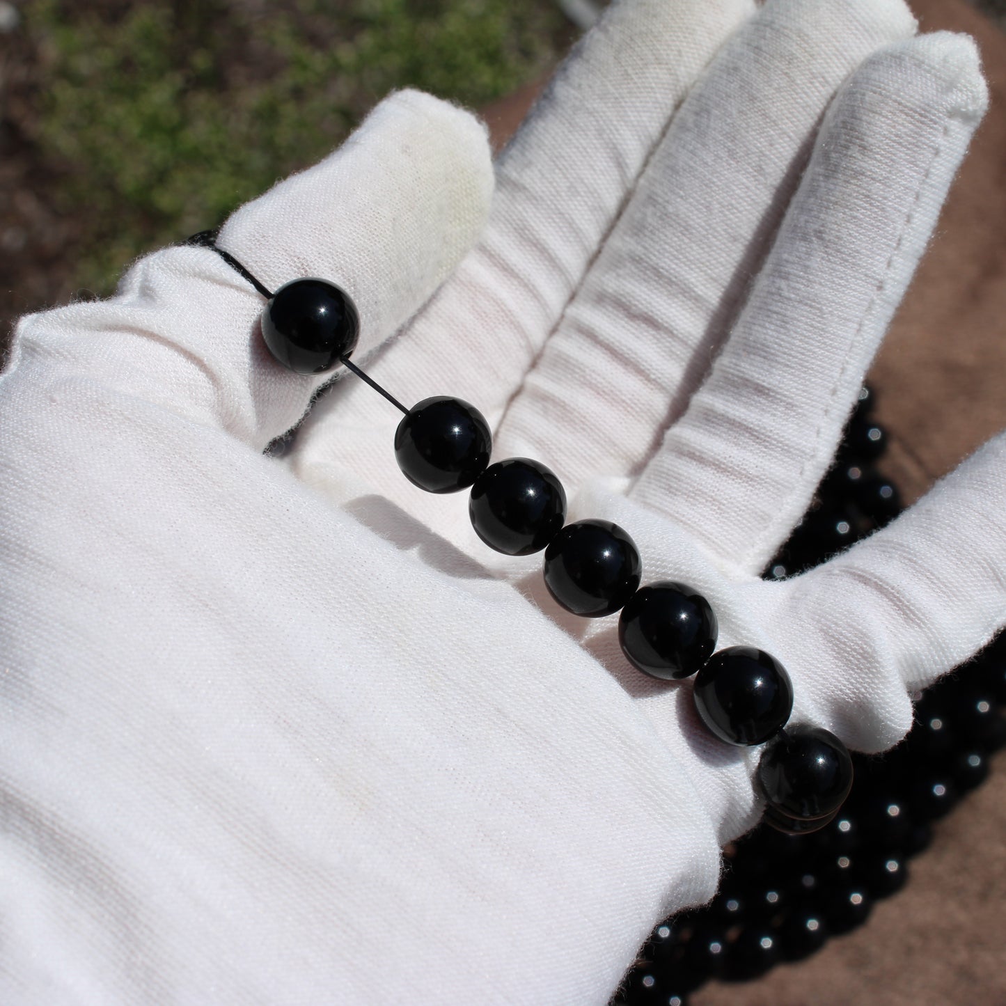 Handmade obsidian bracelet displayed on a gloved hand with polished black beads