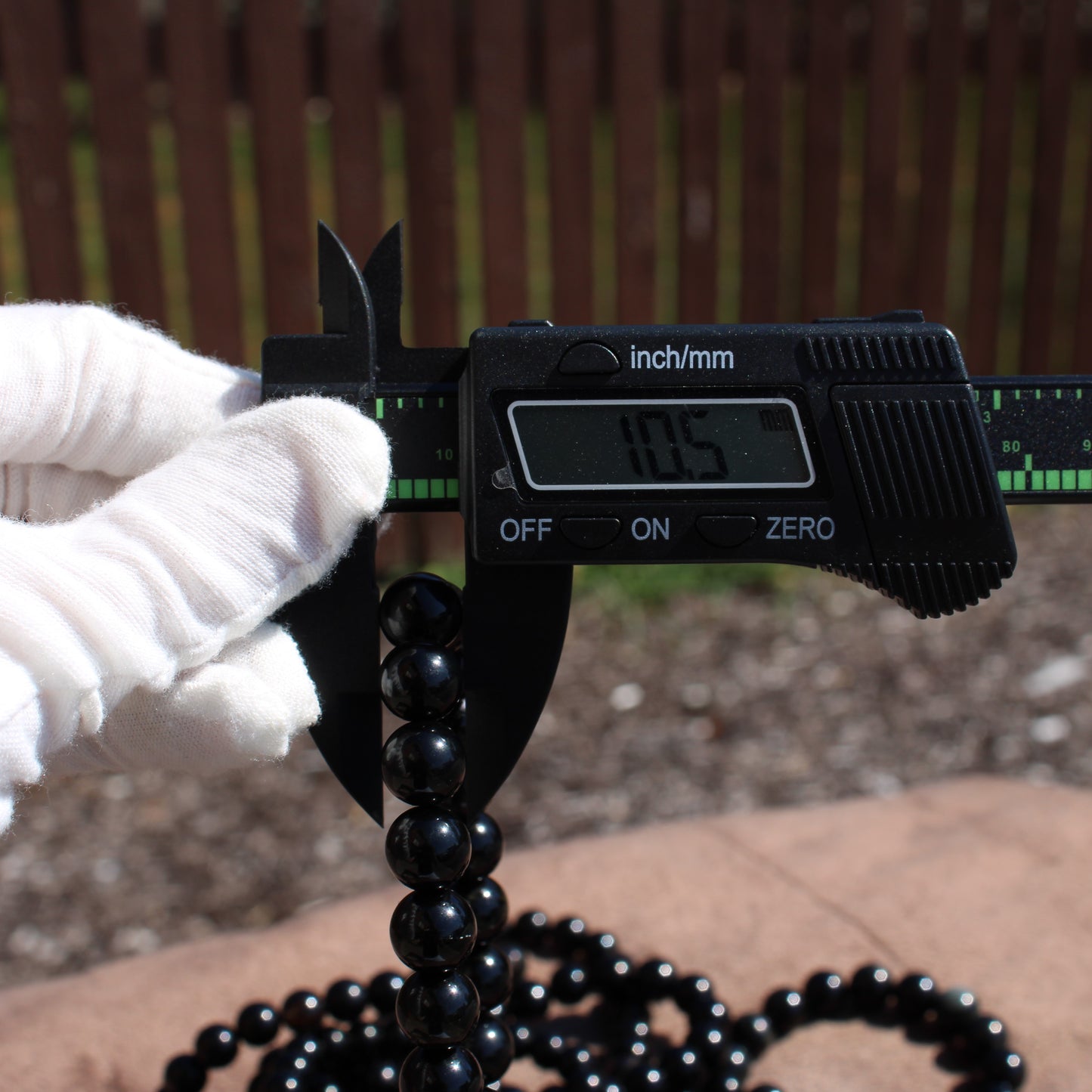 Measuring handmade obsidian bracelet with calipers in a bright outdoor setting