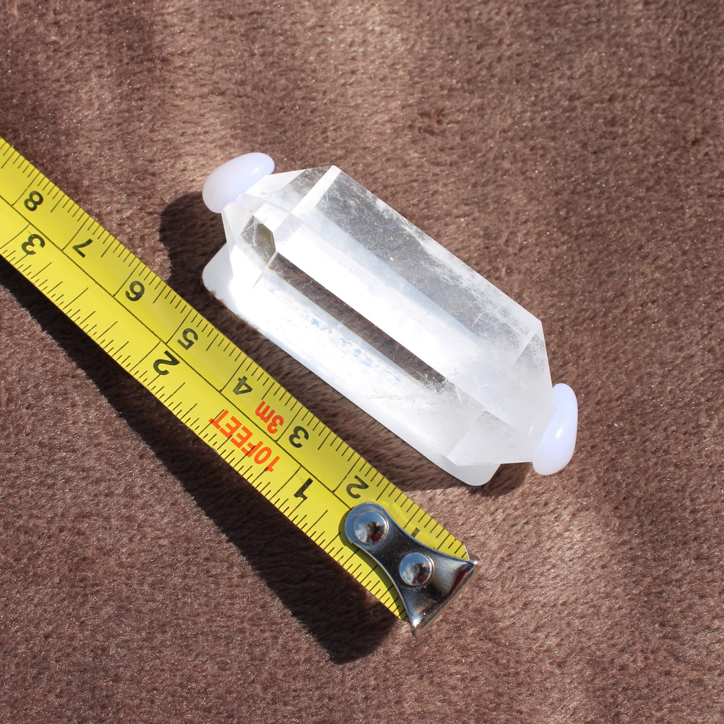 High Quality Clear Quartz crystal from Different Branches LLC next to a measuring tape on brown fabric
