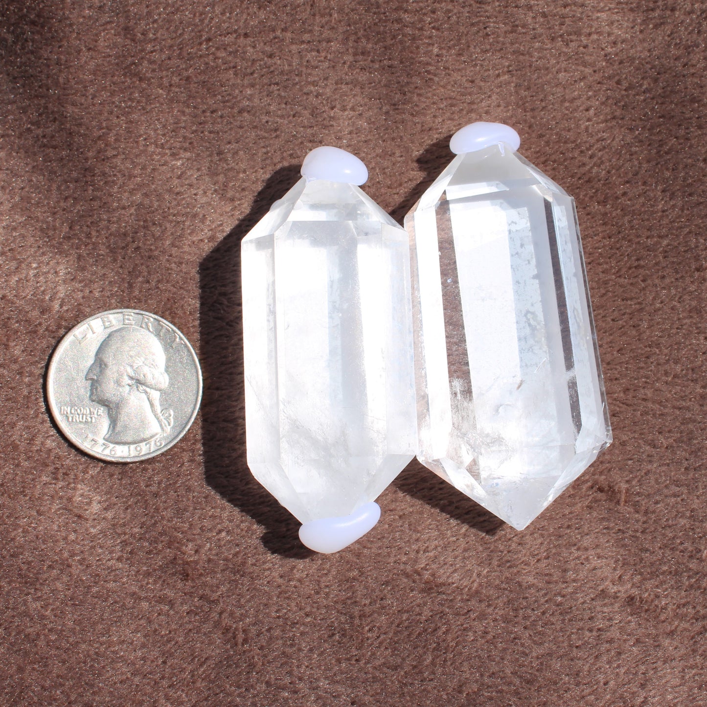 High Quality Clear Quartz crystal points next to a US quarter for size comparison on brown fabric