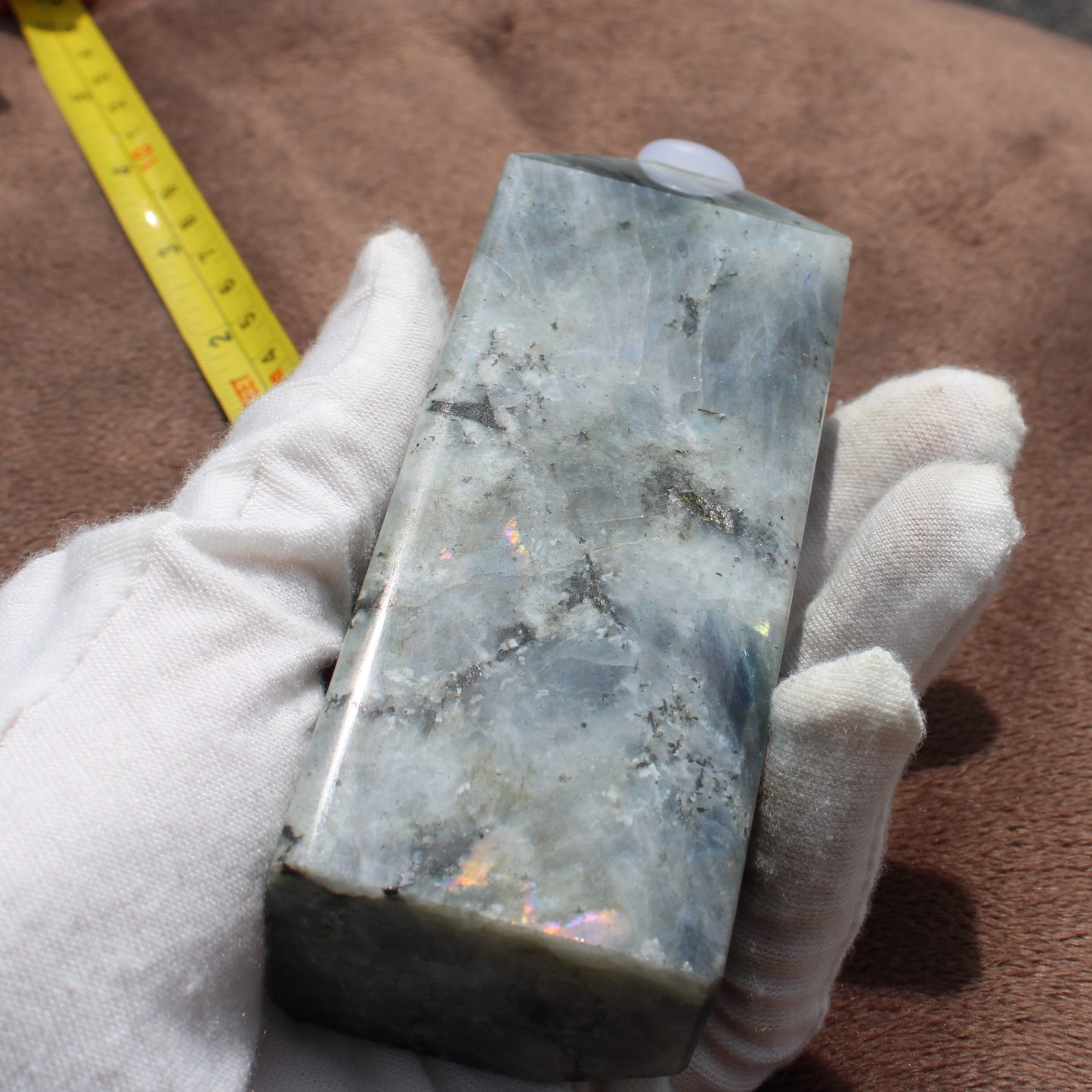 Labradorite Tower crystal held in gloved hand showing its smooth polished surface and iridescent colors