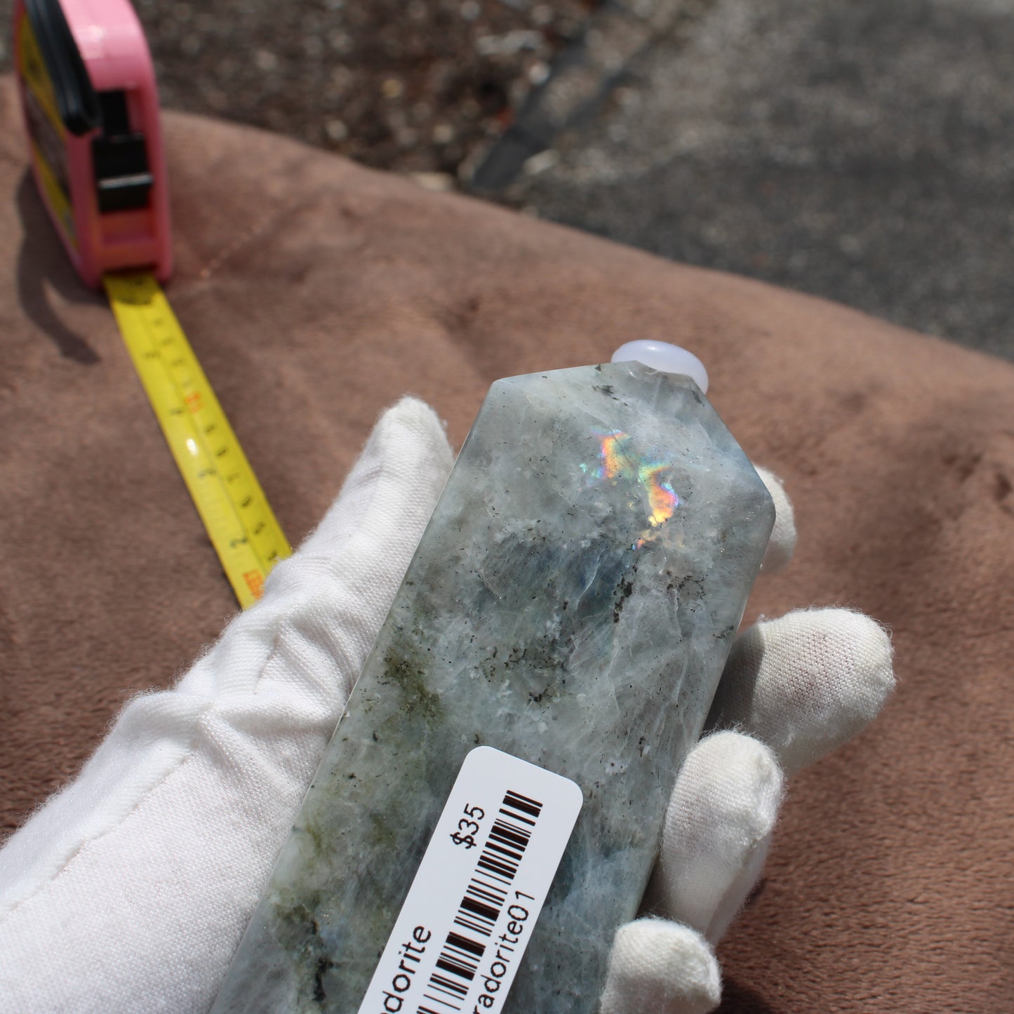 Hand holding a polished Labradorite Tower crystal with a price tag from Different Branches LLC