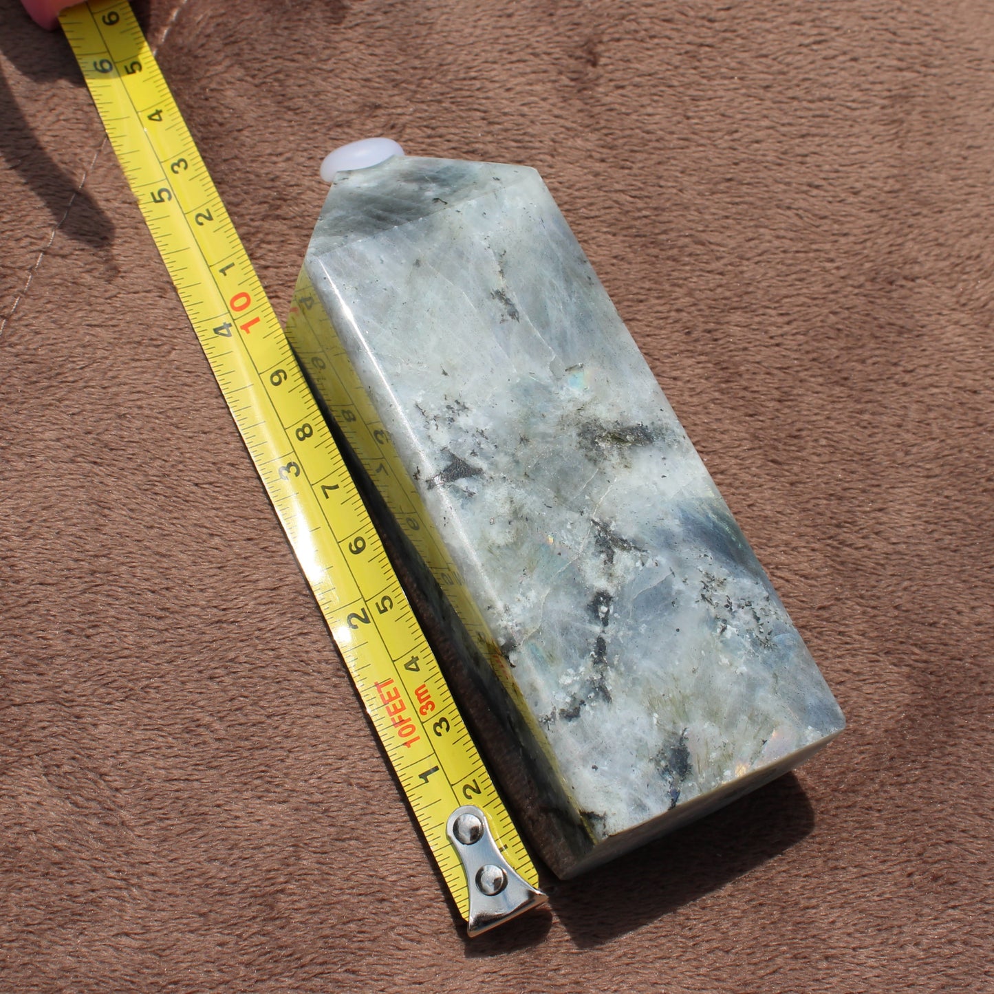 Polished Labradorite Tower crystal next to yellow measuring tape showing size on brown fabric background