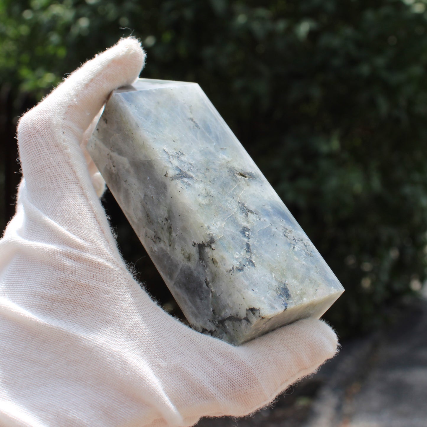 Hand holding a polished Labradorite Tower crystal with natural gray and blue hues outdoors