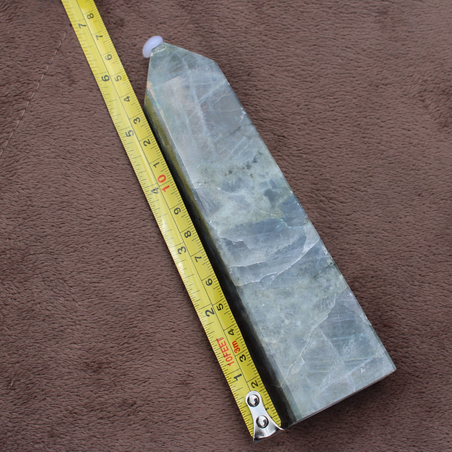 Labradorite Tower crystal standing next to a measuring tape on brown fabric background
