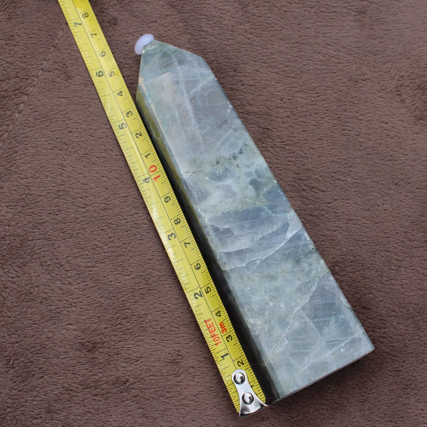 Labradorite Tower crystal standing next to a measuring tape on brown fabric background