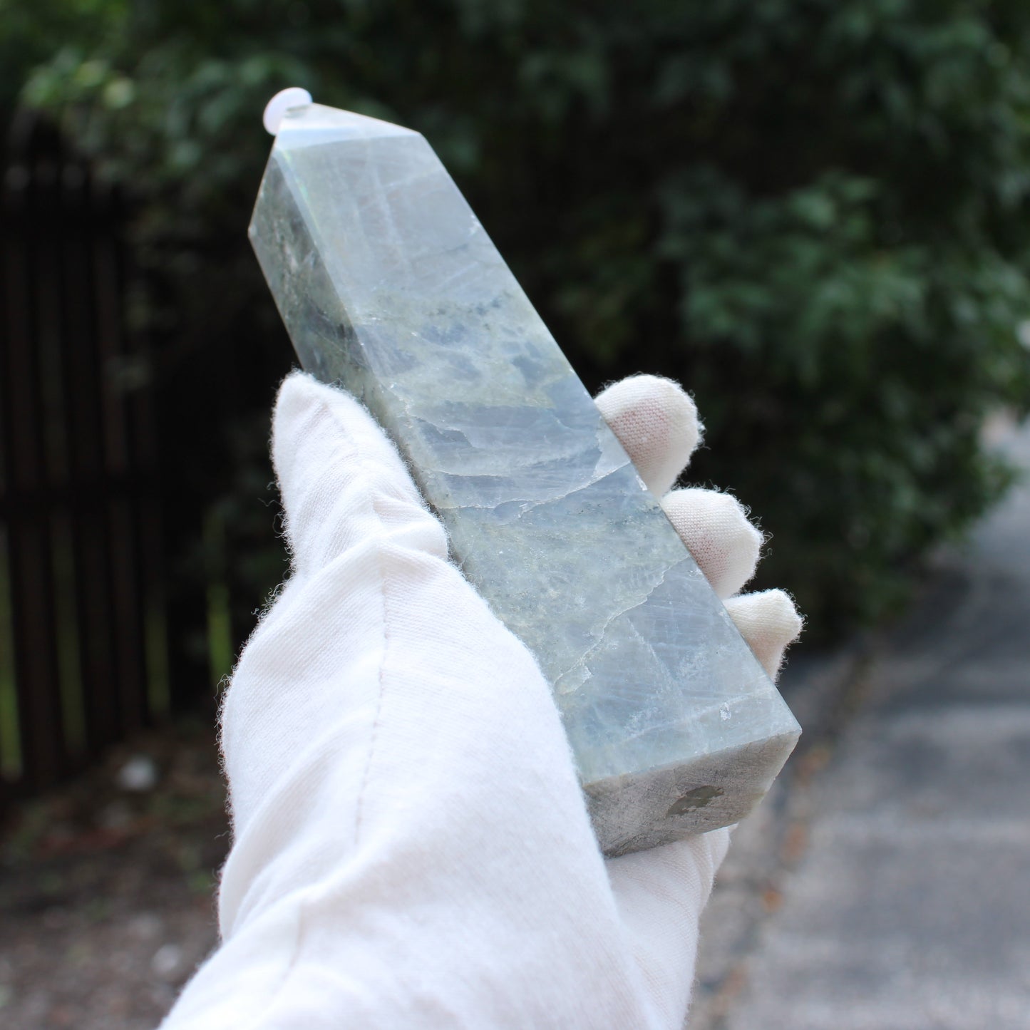 Hand holding a polished Labradorite Tower crystal with white gloves outdoors by Different Branches LLC