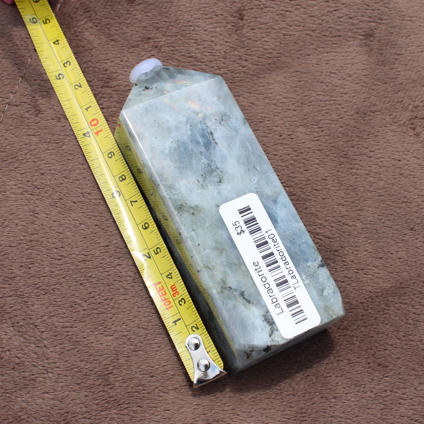 Labradorite Tower crystal from Different Branches LLC shown next to measuring tape on brown fabric