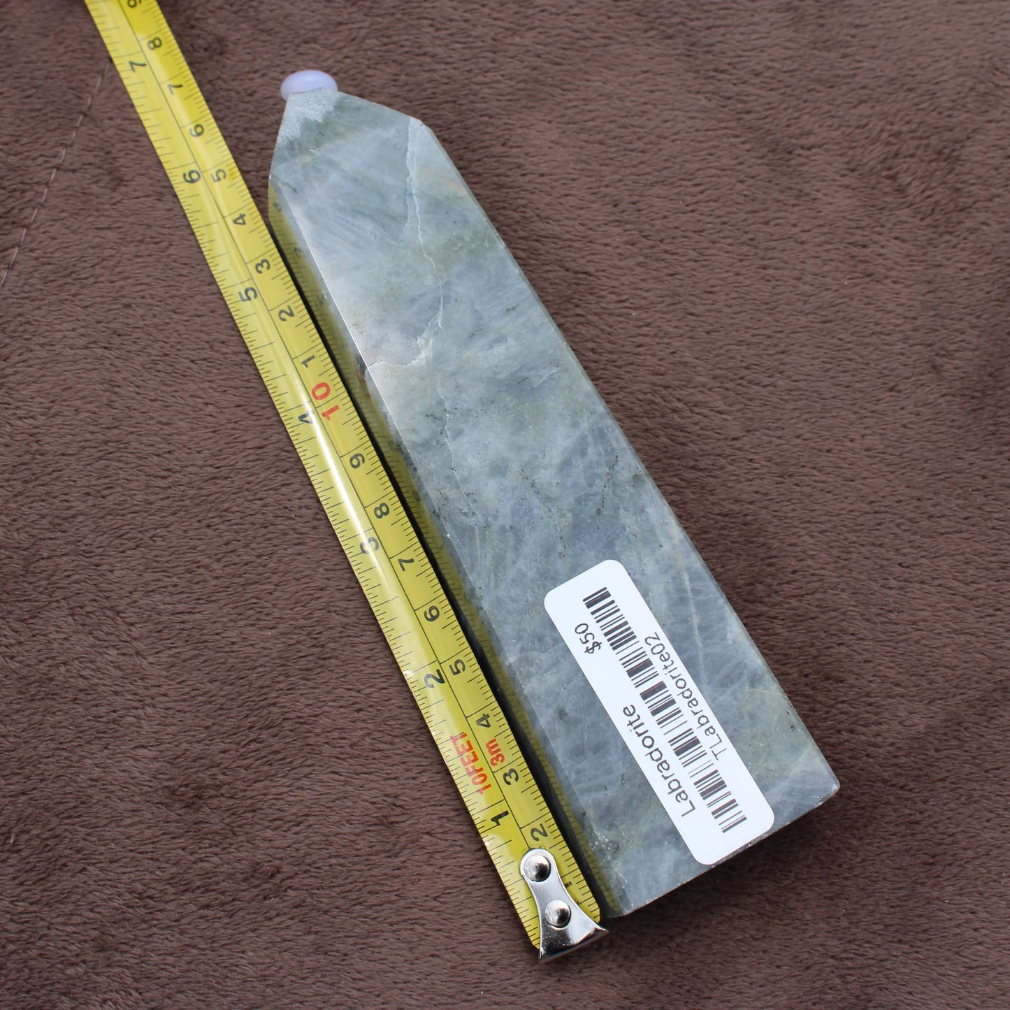 Labradorite Tower crystal from Different Branches LLC placed next to a measuring tape on a brown surface