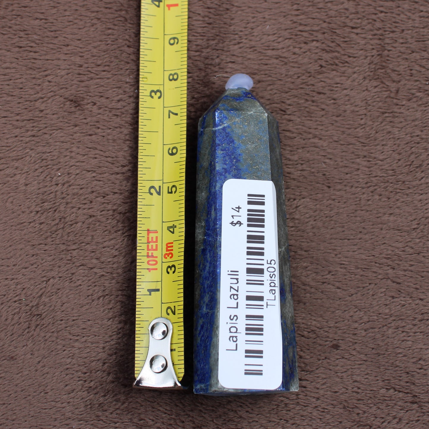Lapiz Lazuli Tower crystal next to measuring tape showing size on brown fabric background