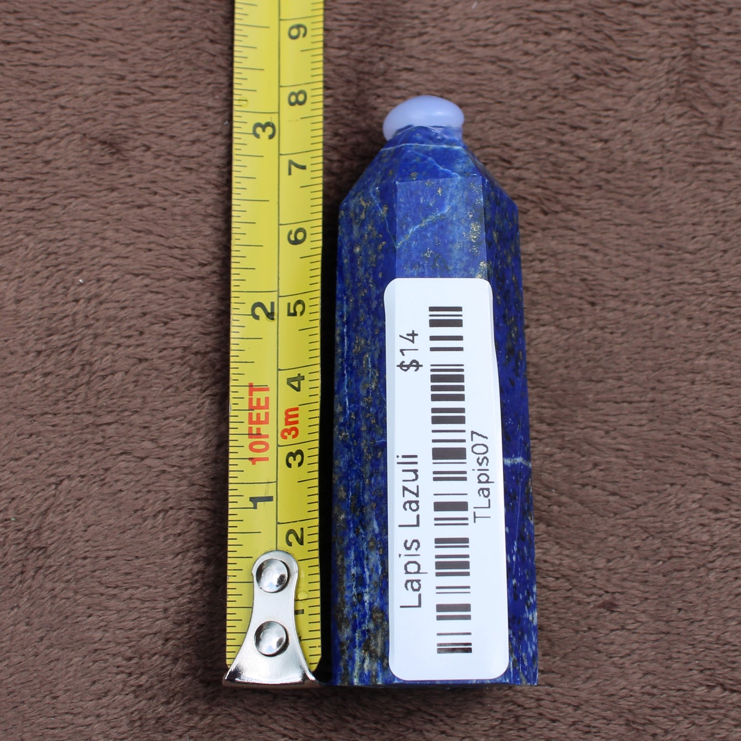Lapiz Lazuli Tower crystal next to a measuring tape showing its size on a brown background