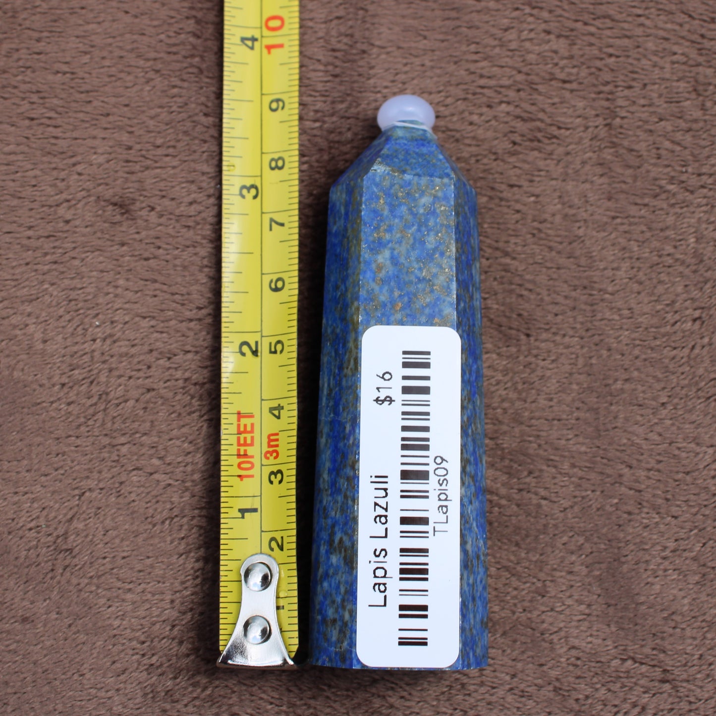 Lapiz Lazuli Tower crystal standing next to a measuring tape showing size on brown fabric background