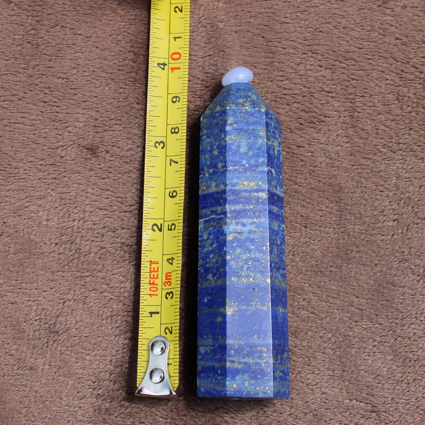 Lapiz Lazuli Tower crystal standing next to measuring tape showing size on brown fabric background