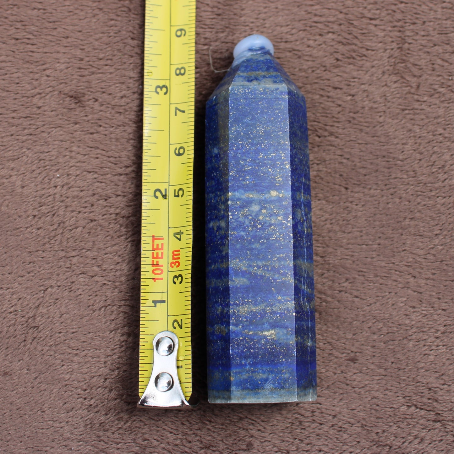 Lapiz Lazuli Tower crystal with deep blue and gold flecks beside a yellow measuring tape