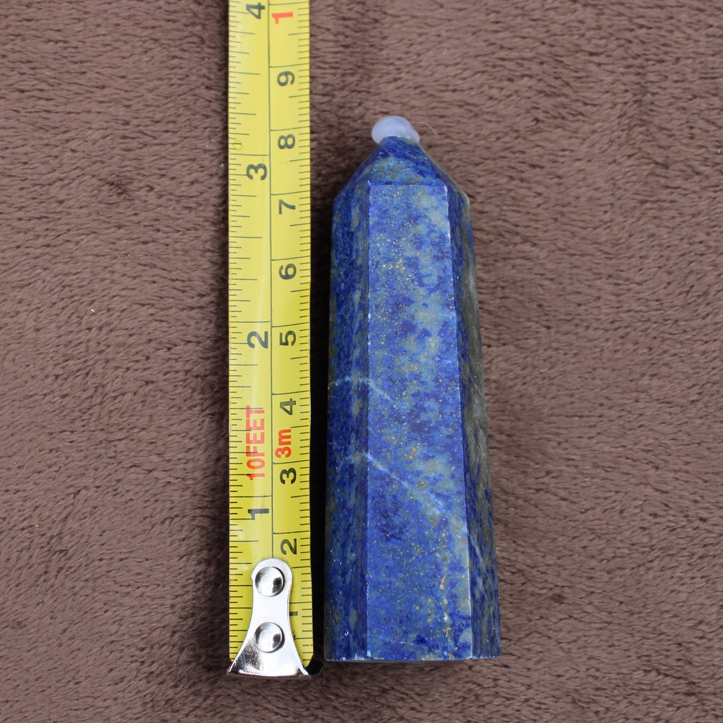 Blue Lapiz Lazuli Tower crystal next to measuring tape showing size on brown fabric background