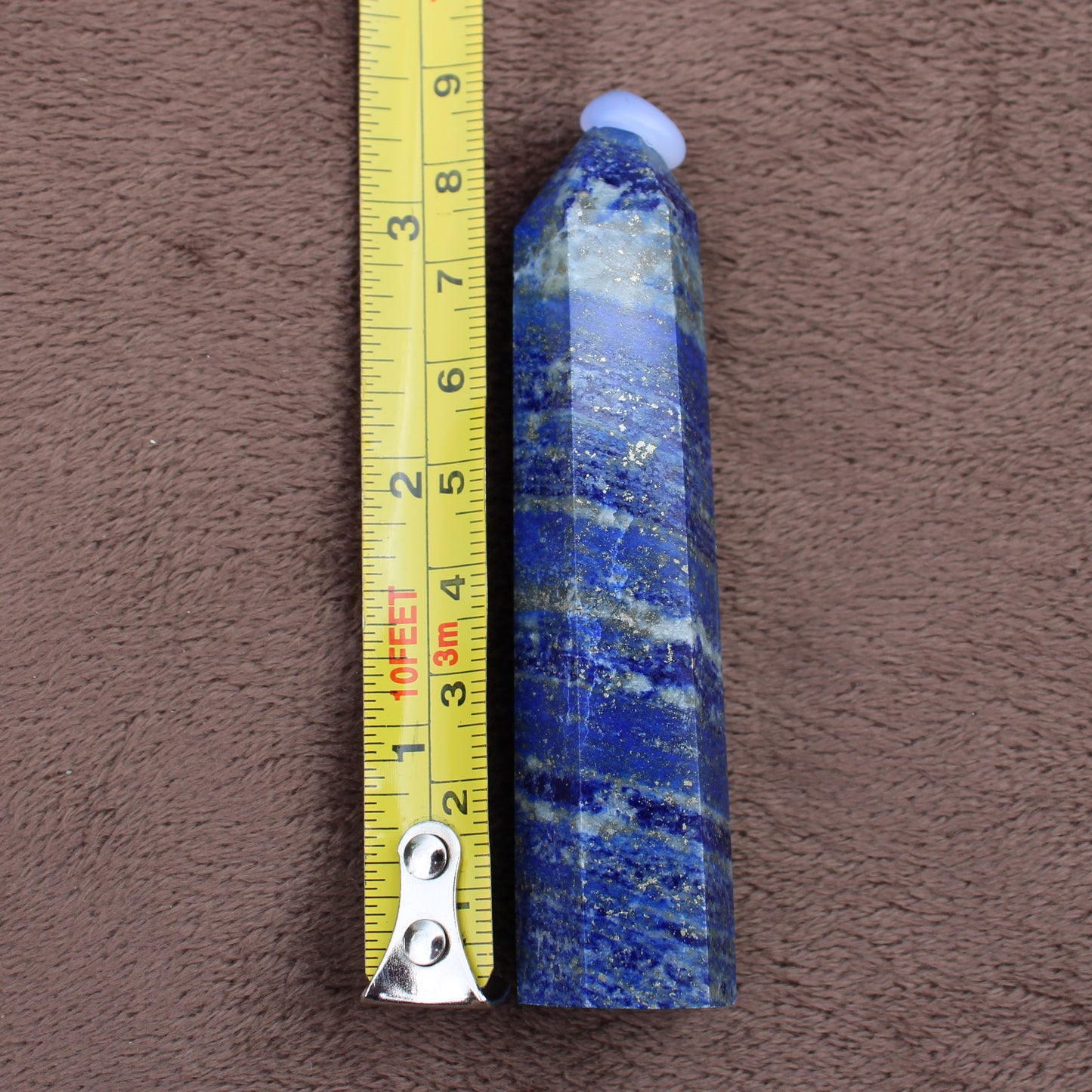 Lapiz Lazuli Tower crystal gemstone next to measuring tape showing size on brown fabric background