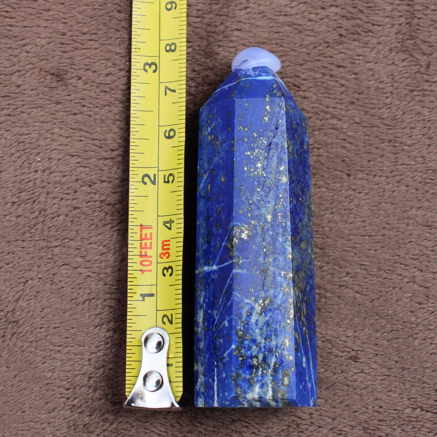 Lapiz Lazuli Tower crystal with deep blue and gold flecks beside a measuring tape on brown fabric