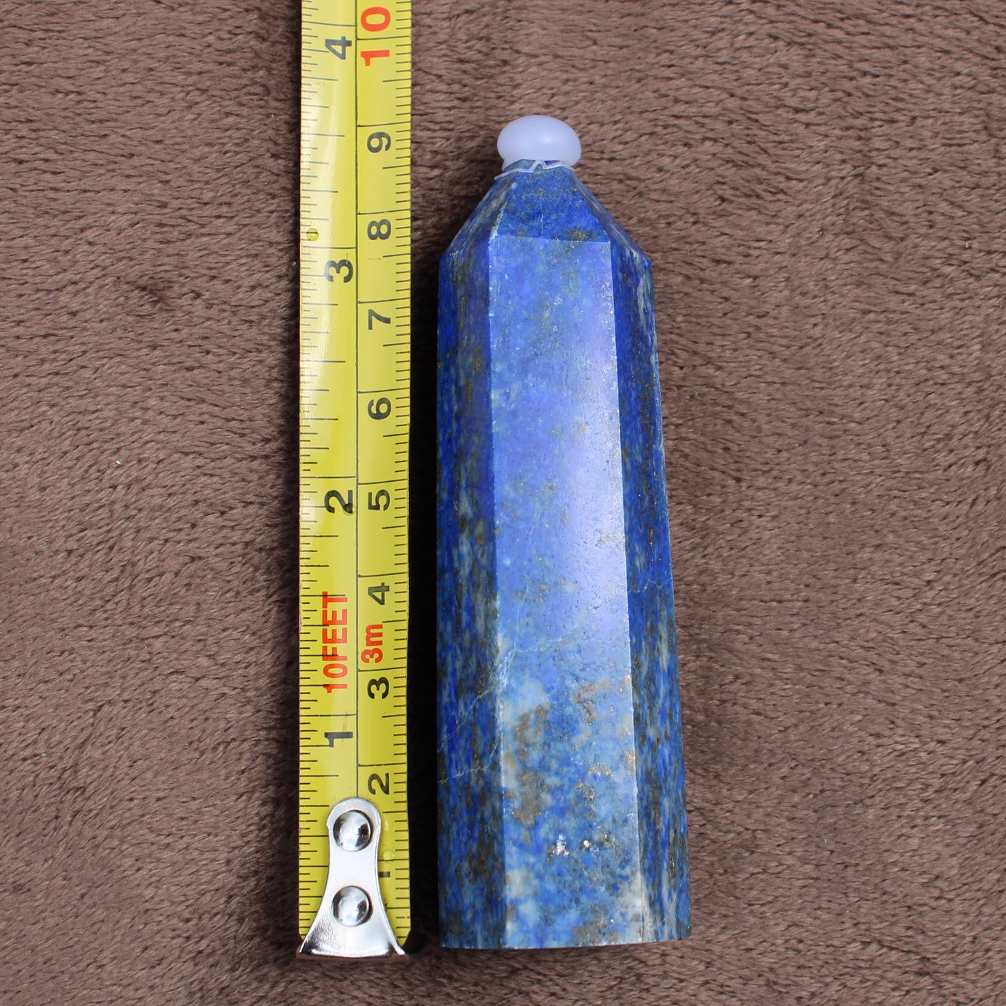Polished Lapiz Lazuli Tower crystal standing next to a measuring tape showing its height