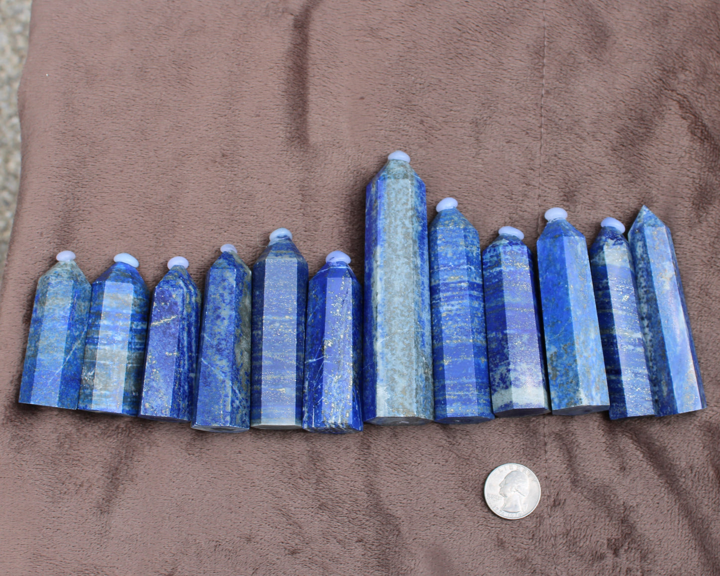 Set of polished blue Lapiz Lazuli Tower crystals displayed on brown fabric with a quarter for size reference