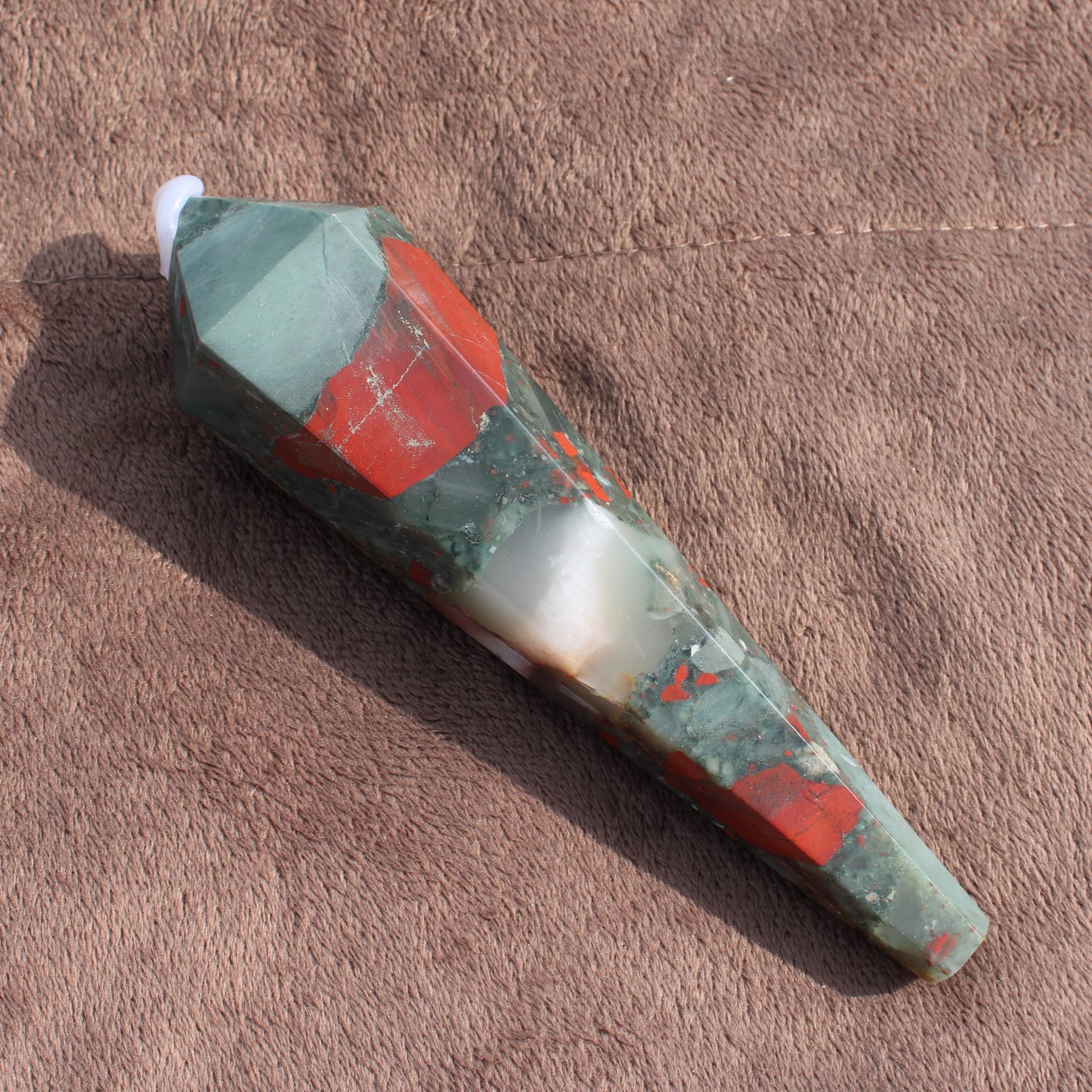 Large Bloodstone Wand crystal with green and red hues on brown fabric background