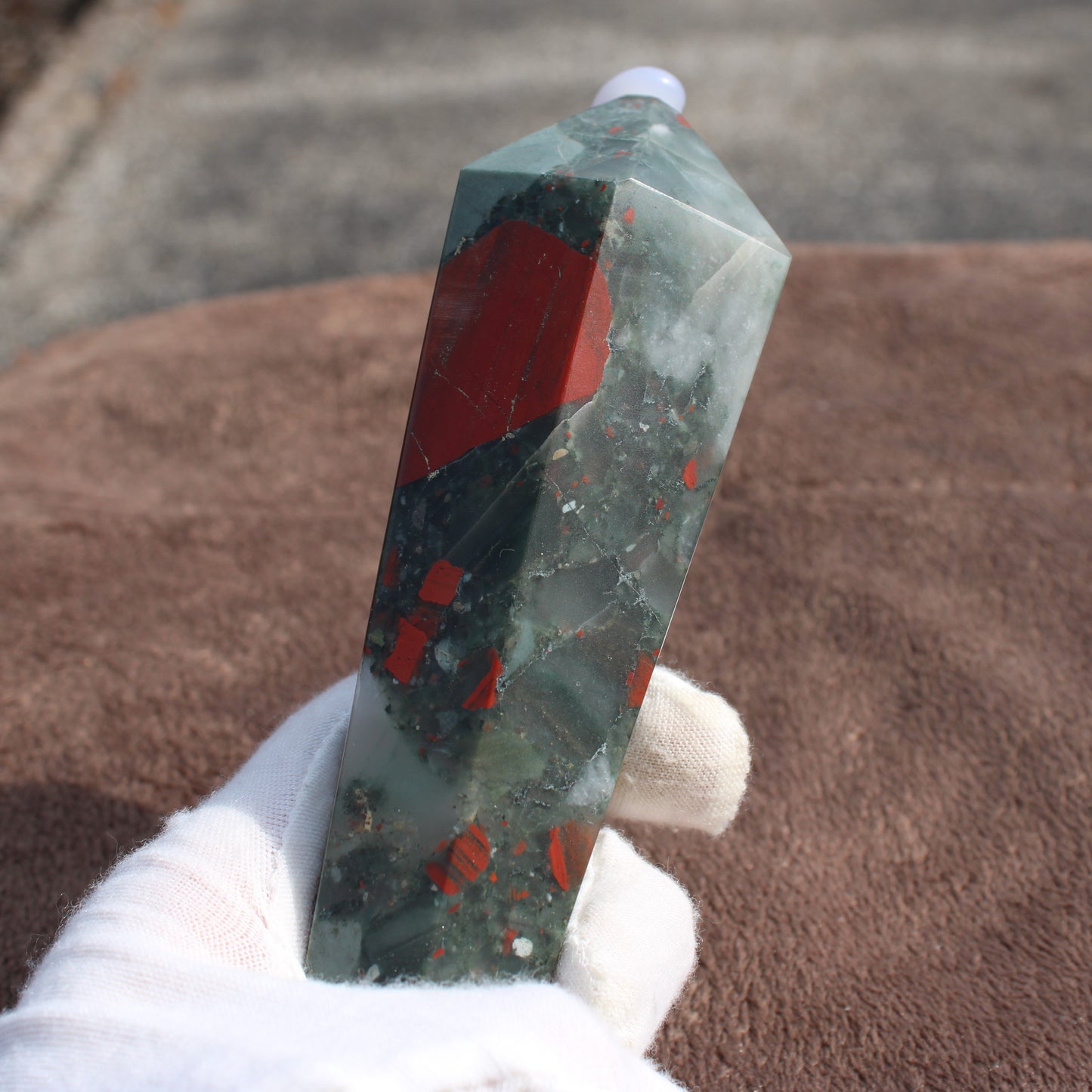 Large Bloodstone Wand crystal with green and red speckles held by a gloved hand by Different Branches LLC