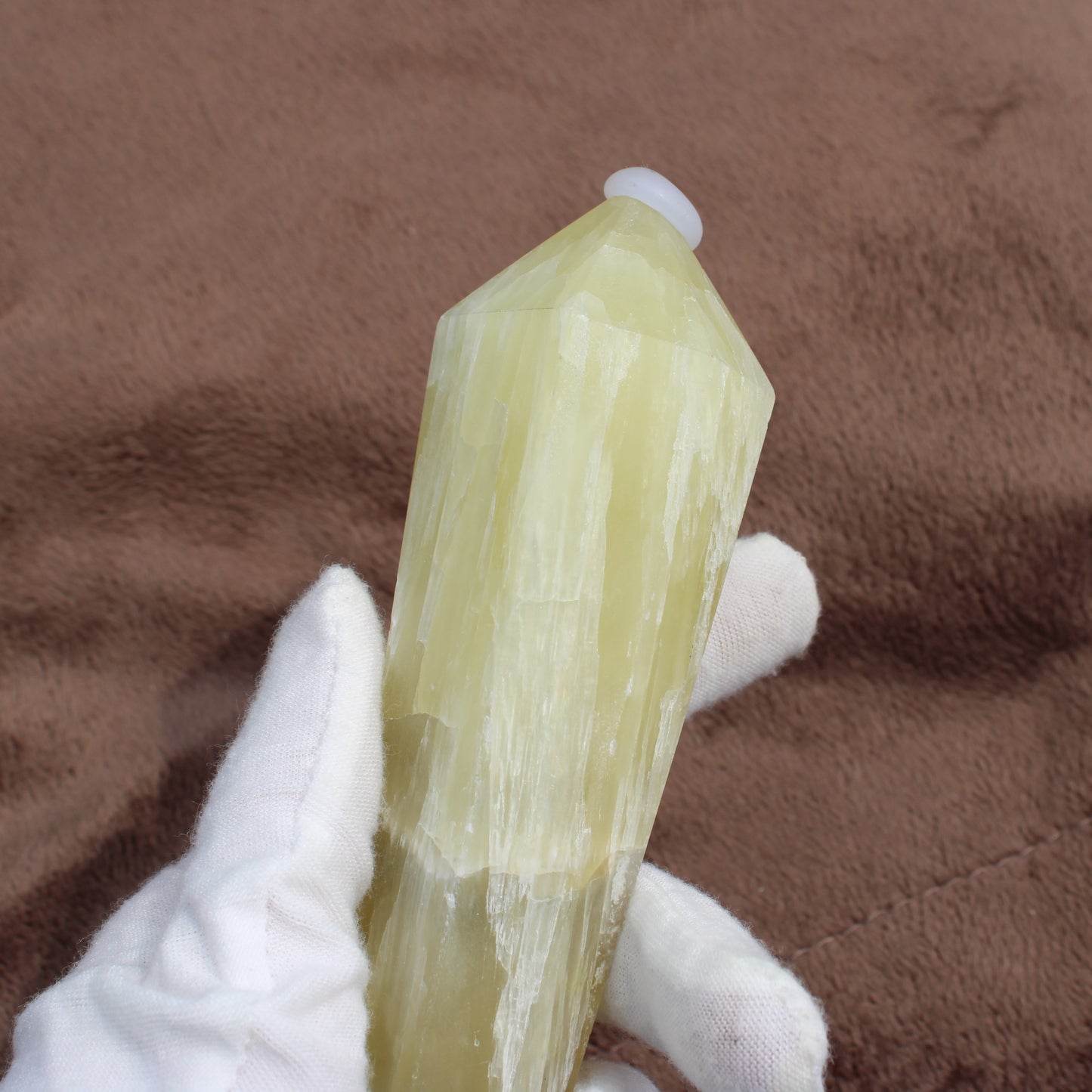 Hand holding a polished Lemon Quartz Wand crystal with a pointed tip on a brown background