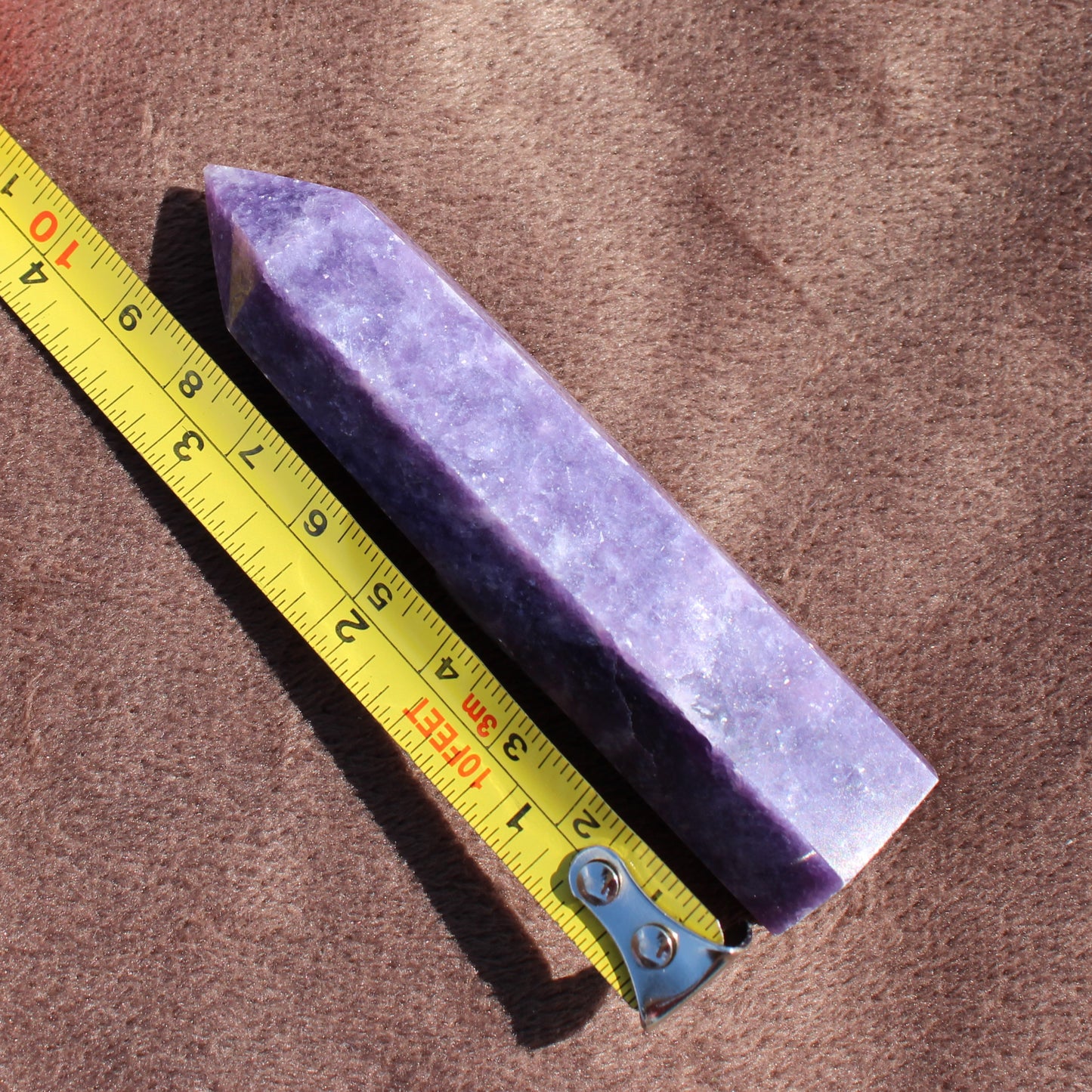Lepidolite Tower crystal next to a yellow measuring tape on a brown surface