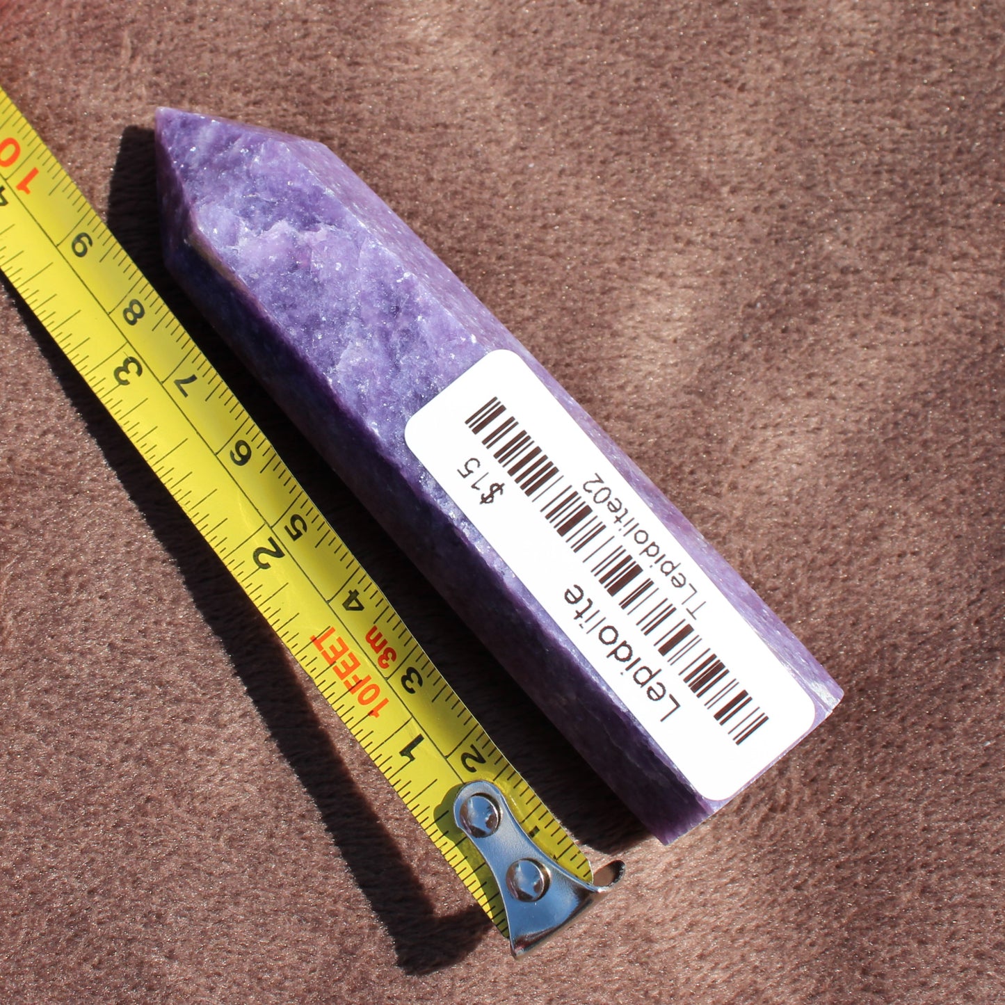 Purple Lepidolite Tower crystal next to a measuring tape showing size for Different Branches LLC