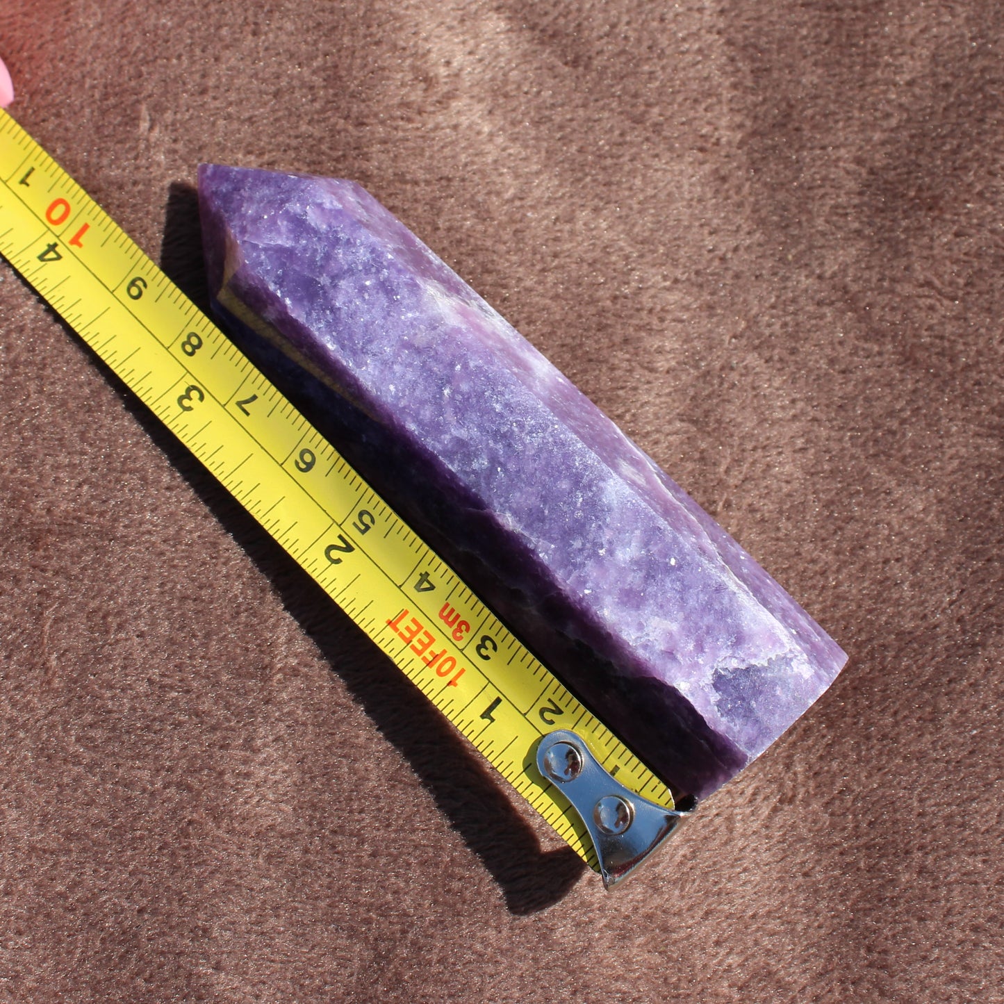 Purple Lepidolite Tower crystal next to yellow measuring tape on brown fabric