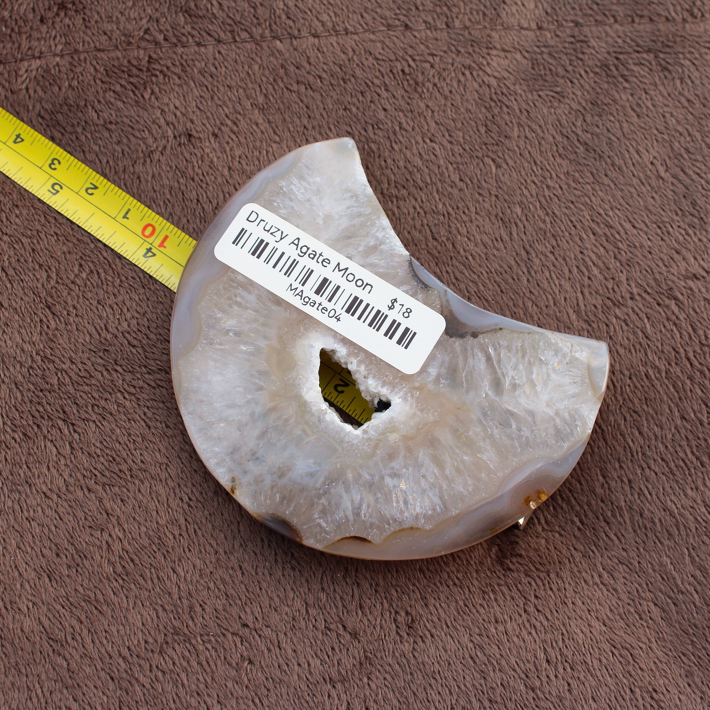 Little Agate Moon crystal with druzy center and ruler for size on brown fabric background