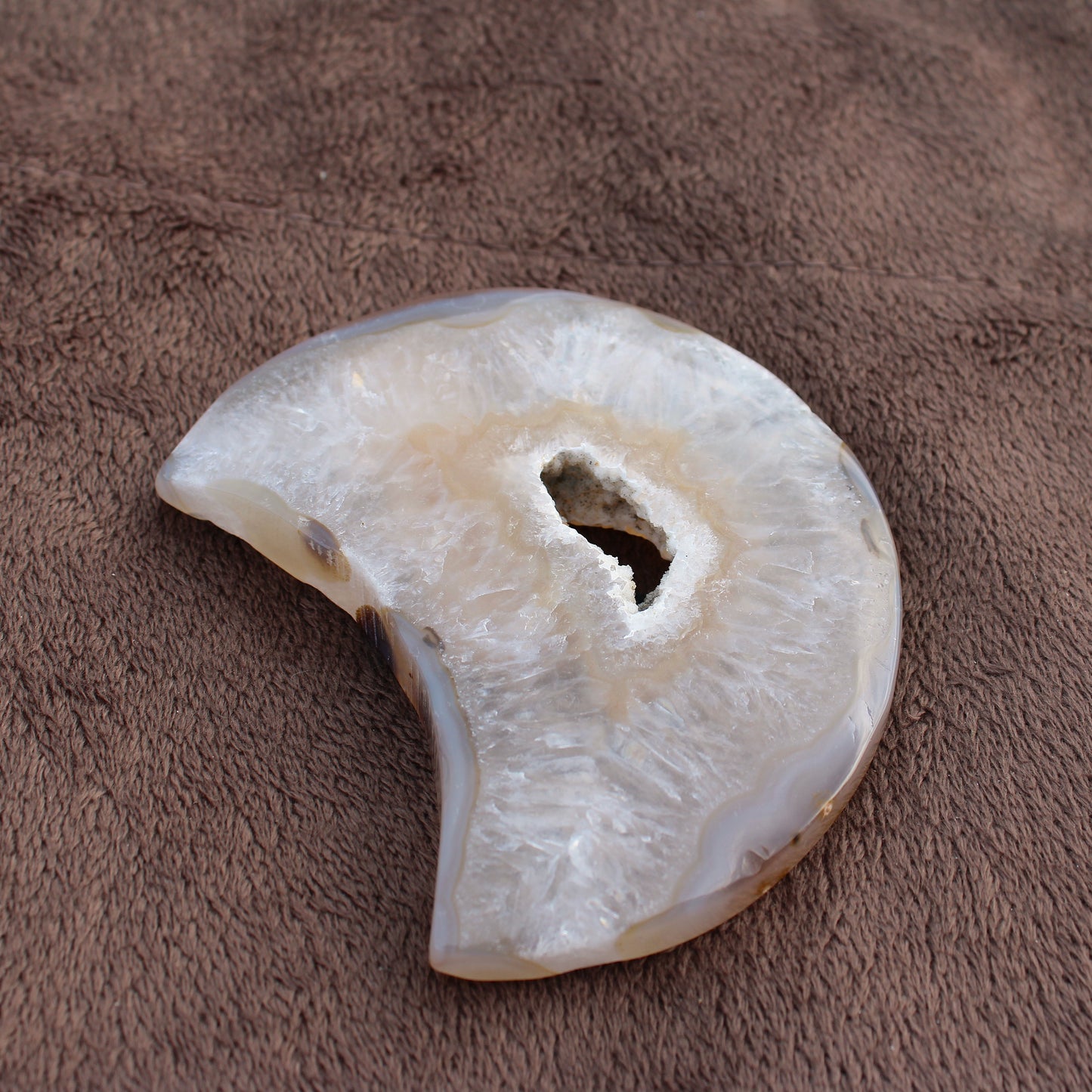 Little Agate Moon crystal with natural translucent white and beige tones on a brown textured surface