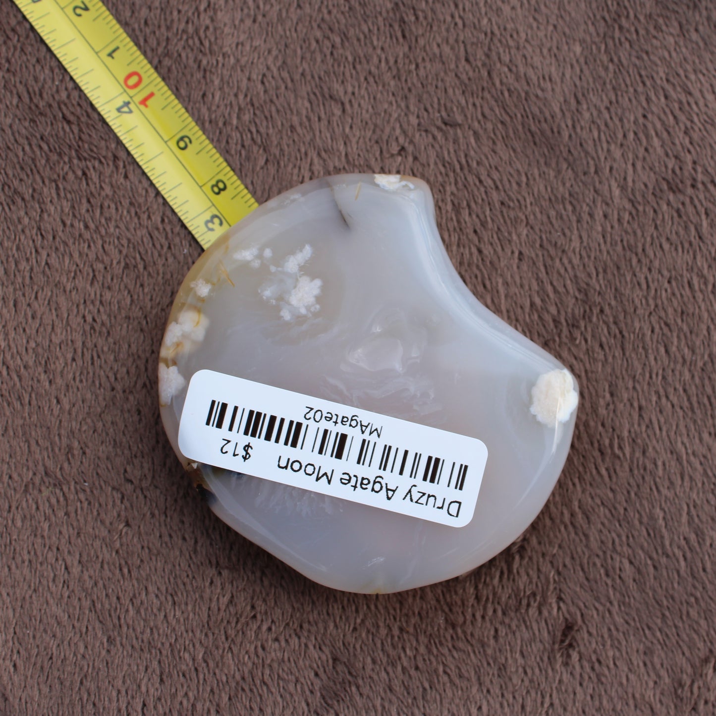Little Agate Moon crystal from Different Branches LLC with milky white and beige patterns shown next to measuring tape