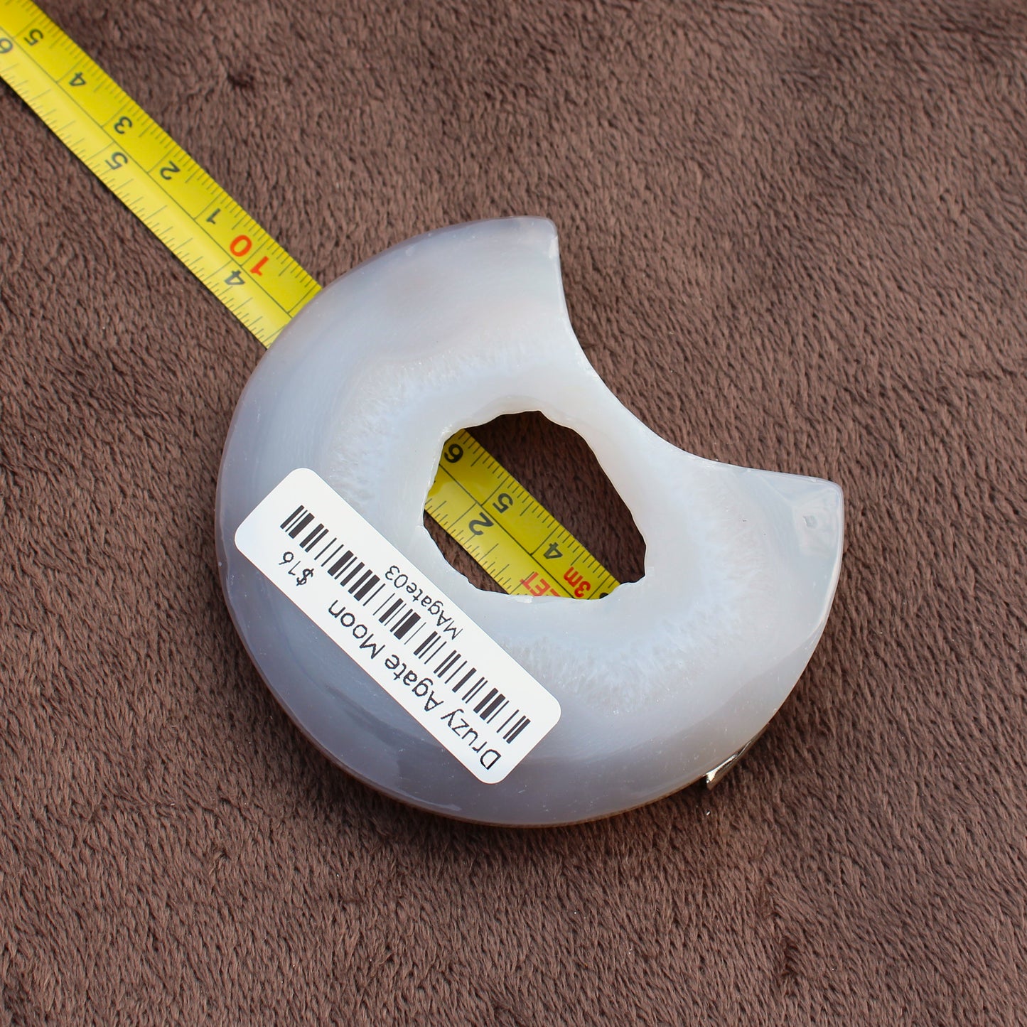 Little Agate Moon crystal from Different Branches LLC shown next to measuring tape on brown fabric