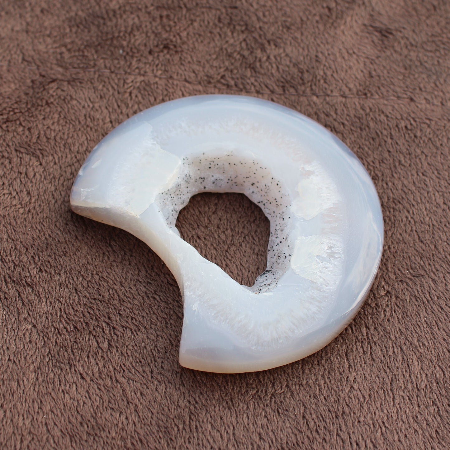 Different Branches LLC Little Agate Moon crystal with translucent white and gray patterns on brown fabric