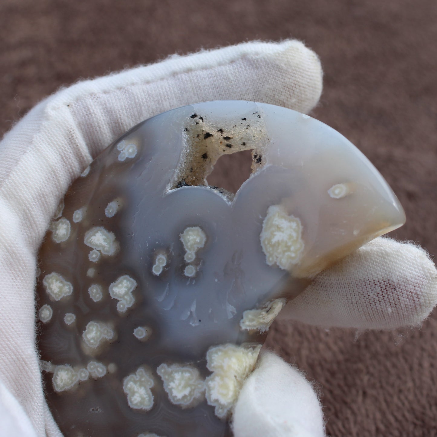 Little Agate Moon crystal with translucent gray and white patterns held in a gloved hand