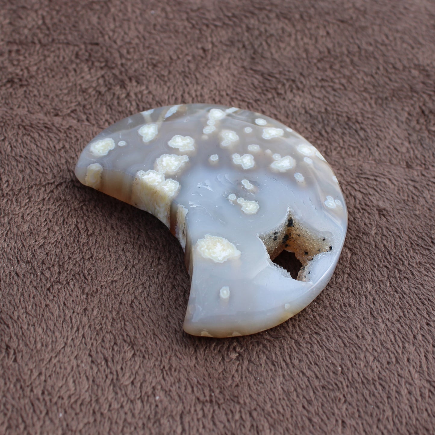 Little Agate Moon crystal with natural white patterns and star-shaped hole on brown fabric
