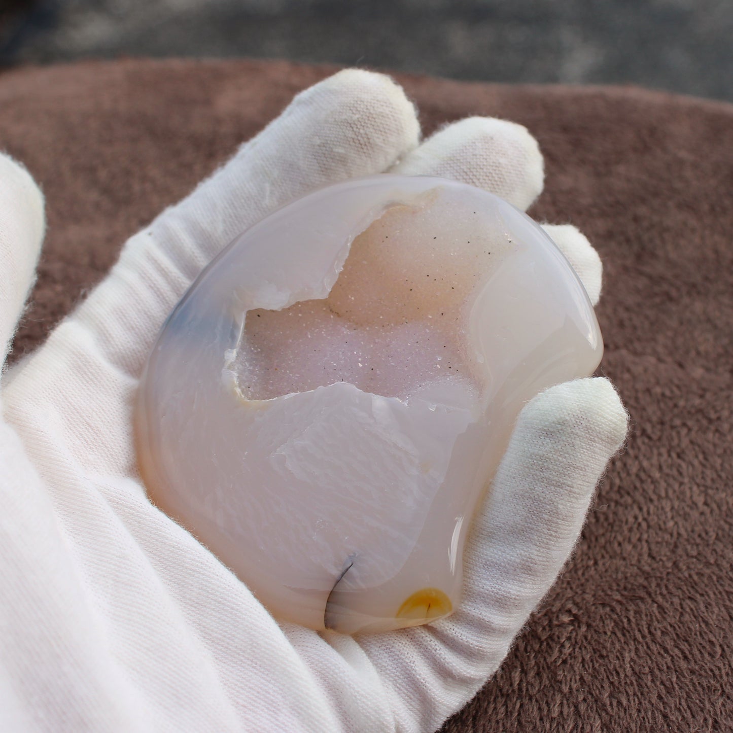 Hand holding a polished Little Agate Moon crystal with natural druzy and soft pastel colors