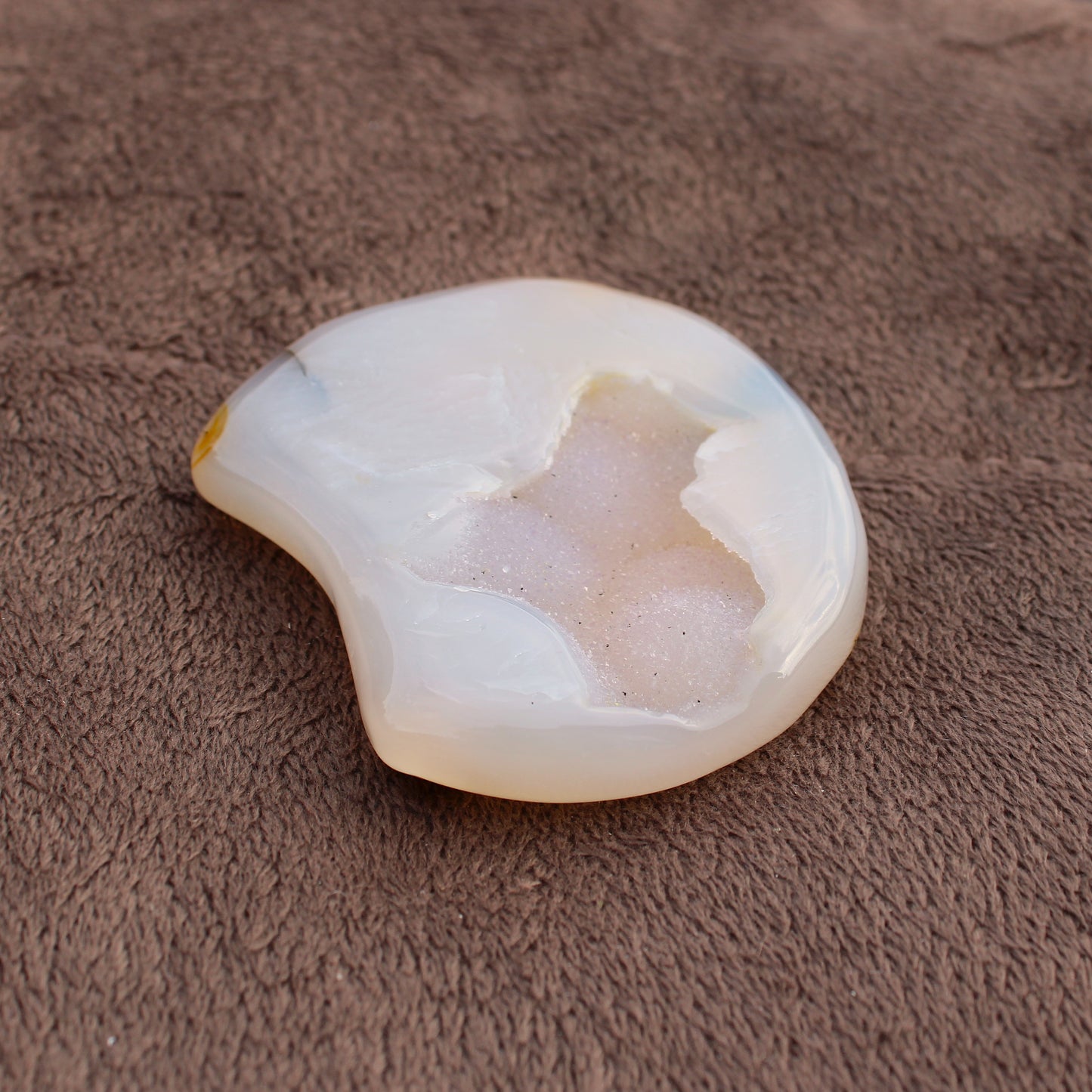 Different Branches LLC Little Agate Moon crystal with white and beige tones on brown fabric