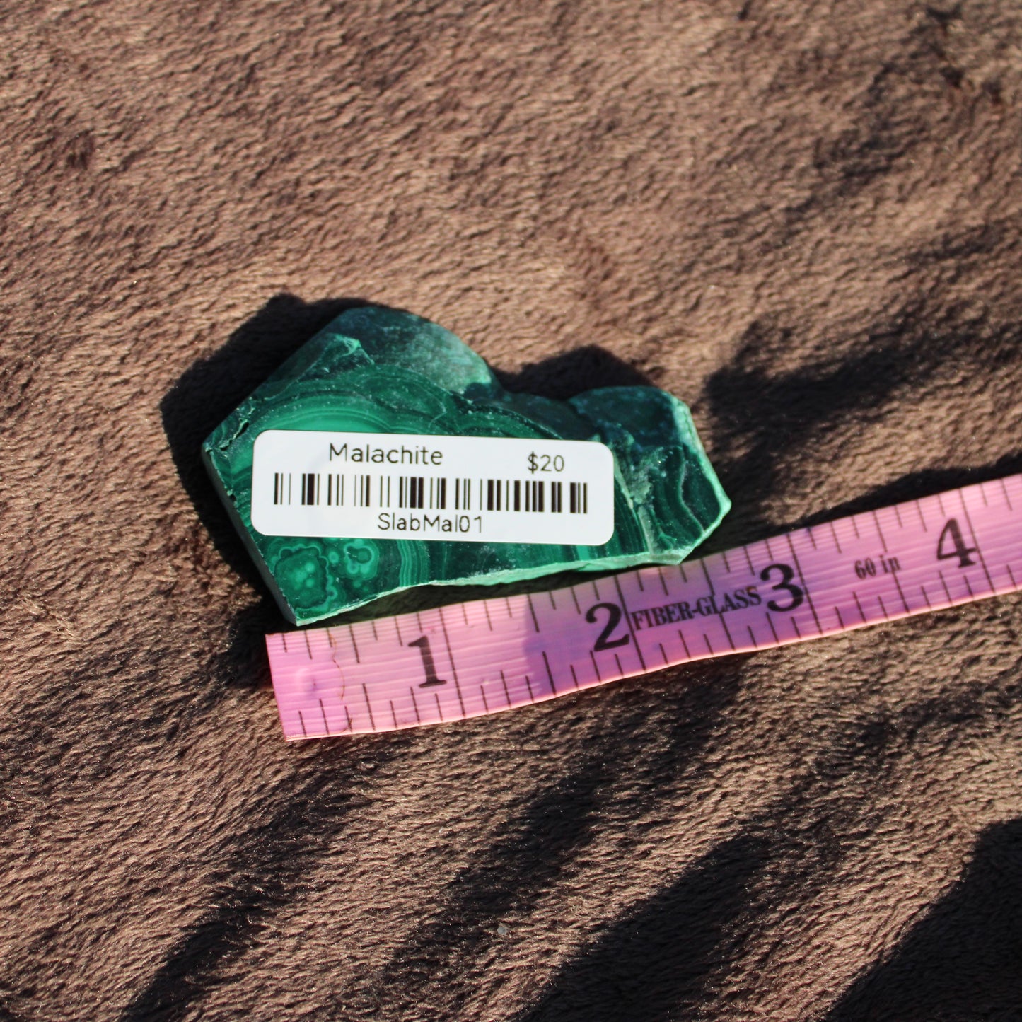 Malachite slab displayed on a soft surface with a price tag and ruler for size reference