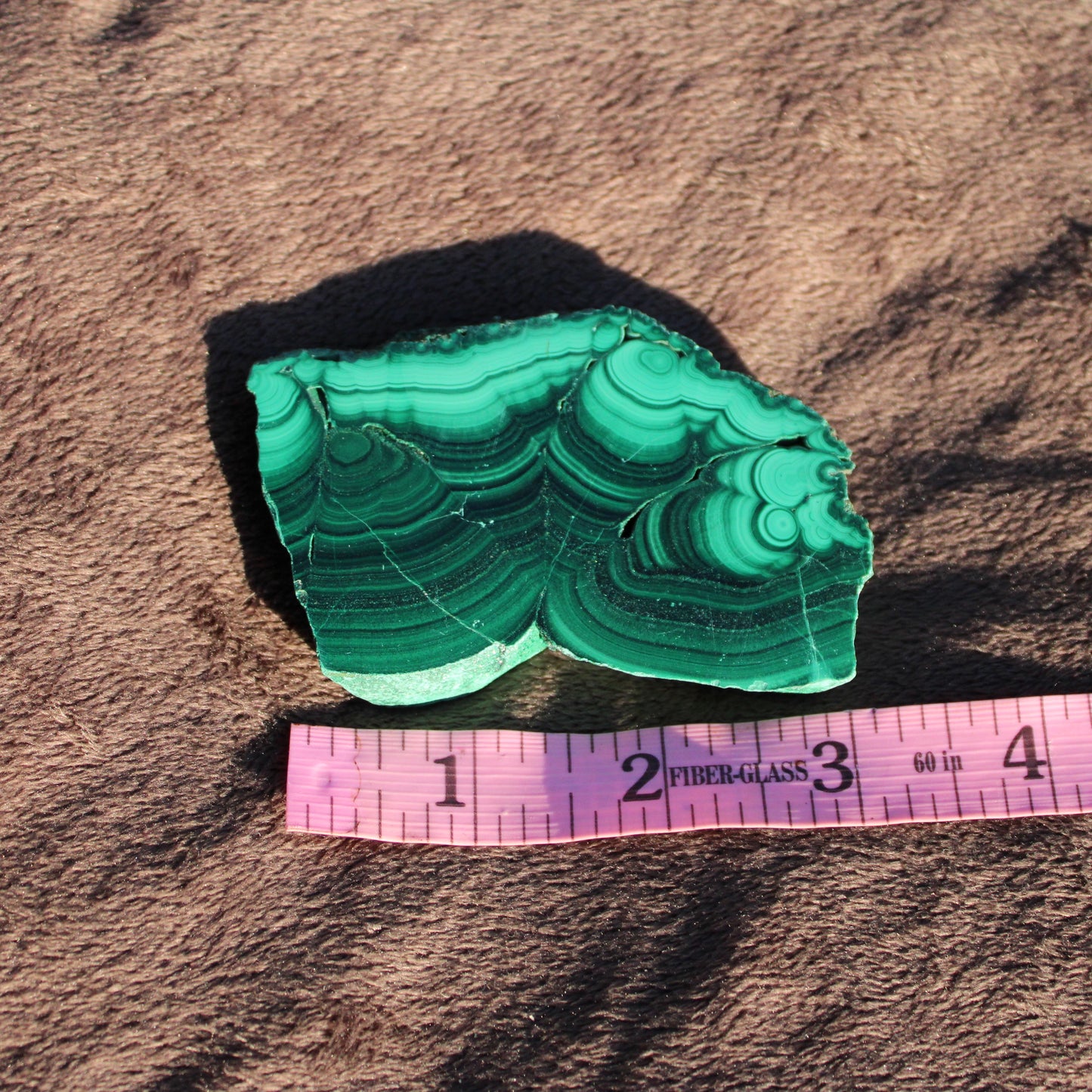 Natural malachite slab with unique green patterns and texture on a measuring tape backdrop