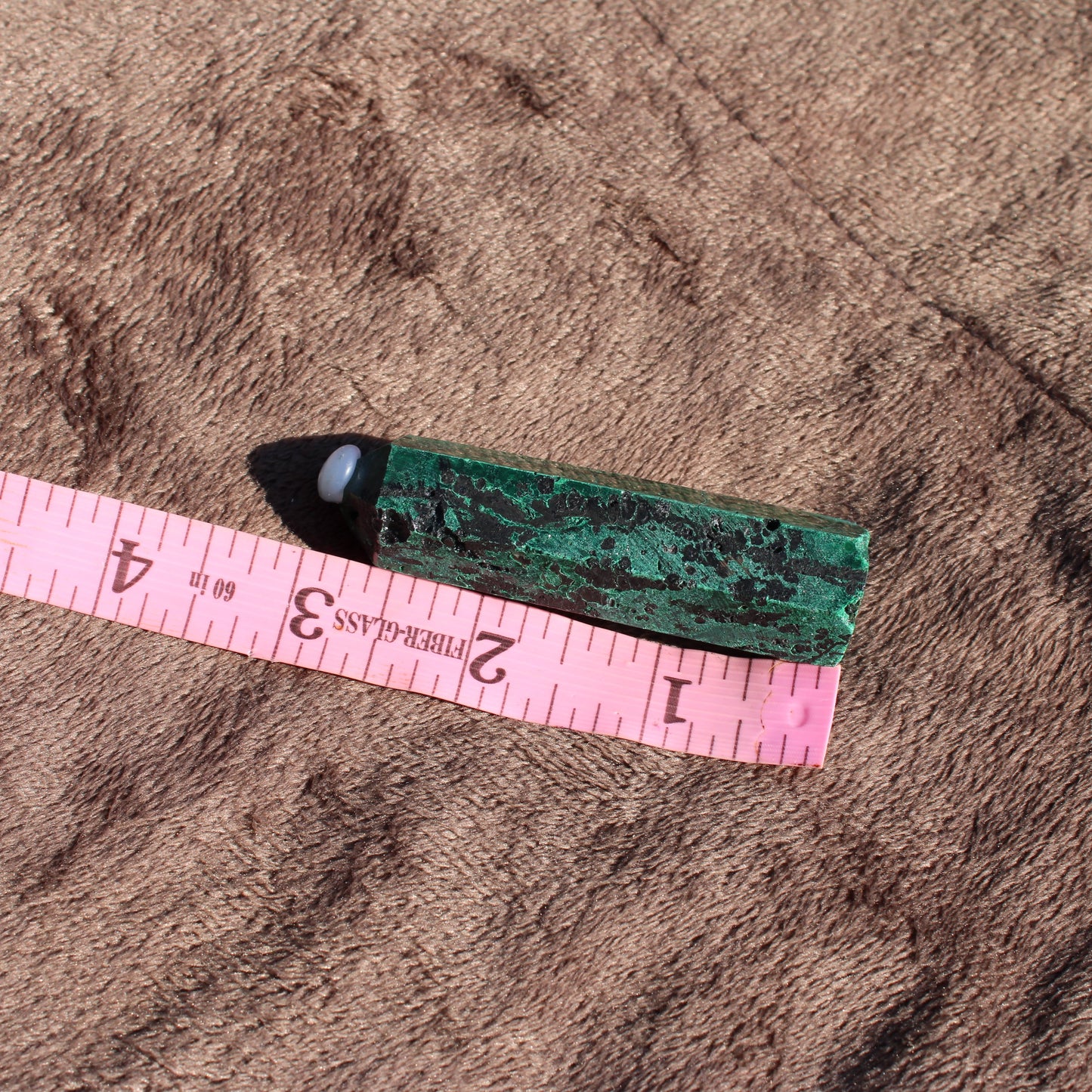 Malachite tower collection showcasing a polished green crystal with a smooth tip and ruler for size reference