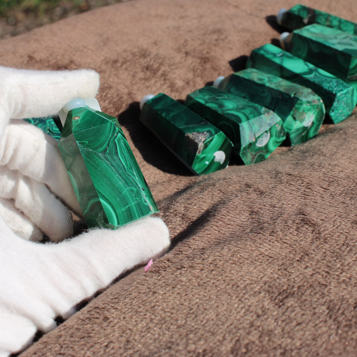 Hand holding a shimmering Malachite tower from the Malachite tower collection on a soft surface